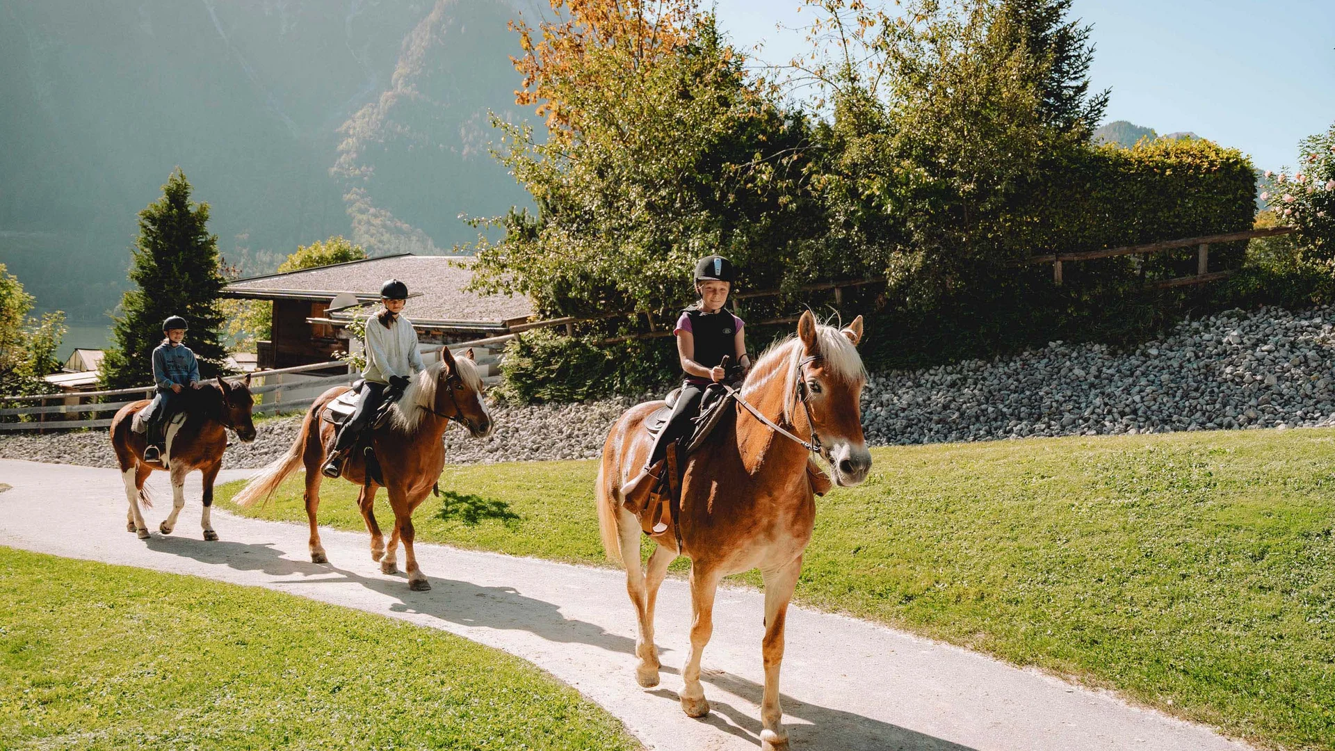 Ihr Familienhotel in Österreich mit All-inclusive-Angebot Drei Kinder reiten auf Pferden auf einem Weg vor einer Berglandschaft