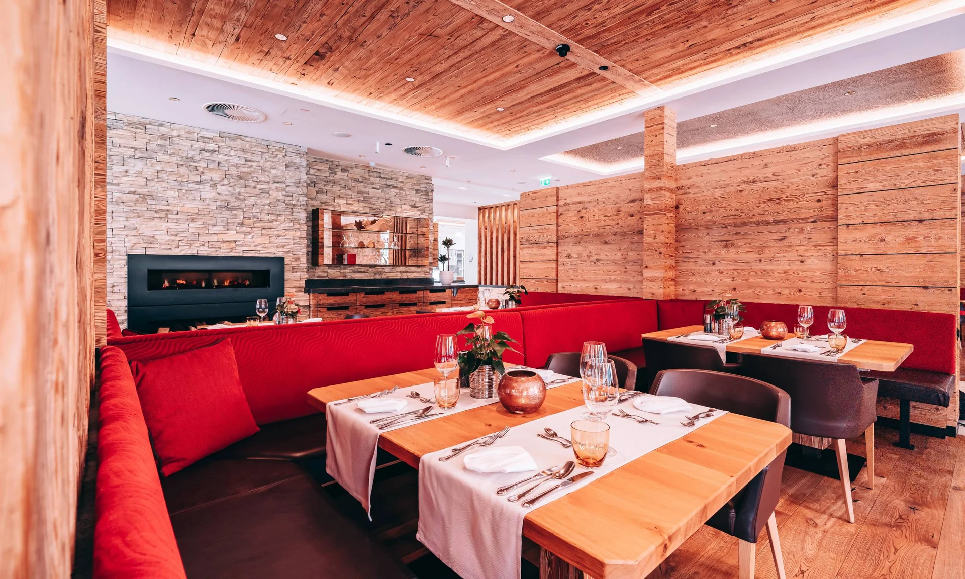 Welcome to our family hotel at Lake Achensee. Modern restaurant with red benches, wooden tables, and a fireplace