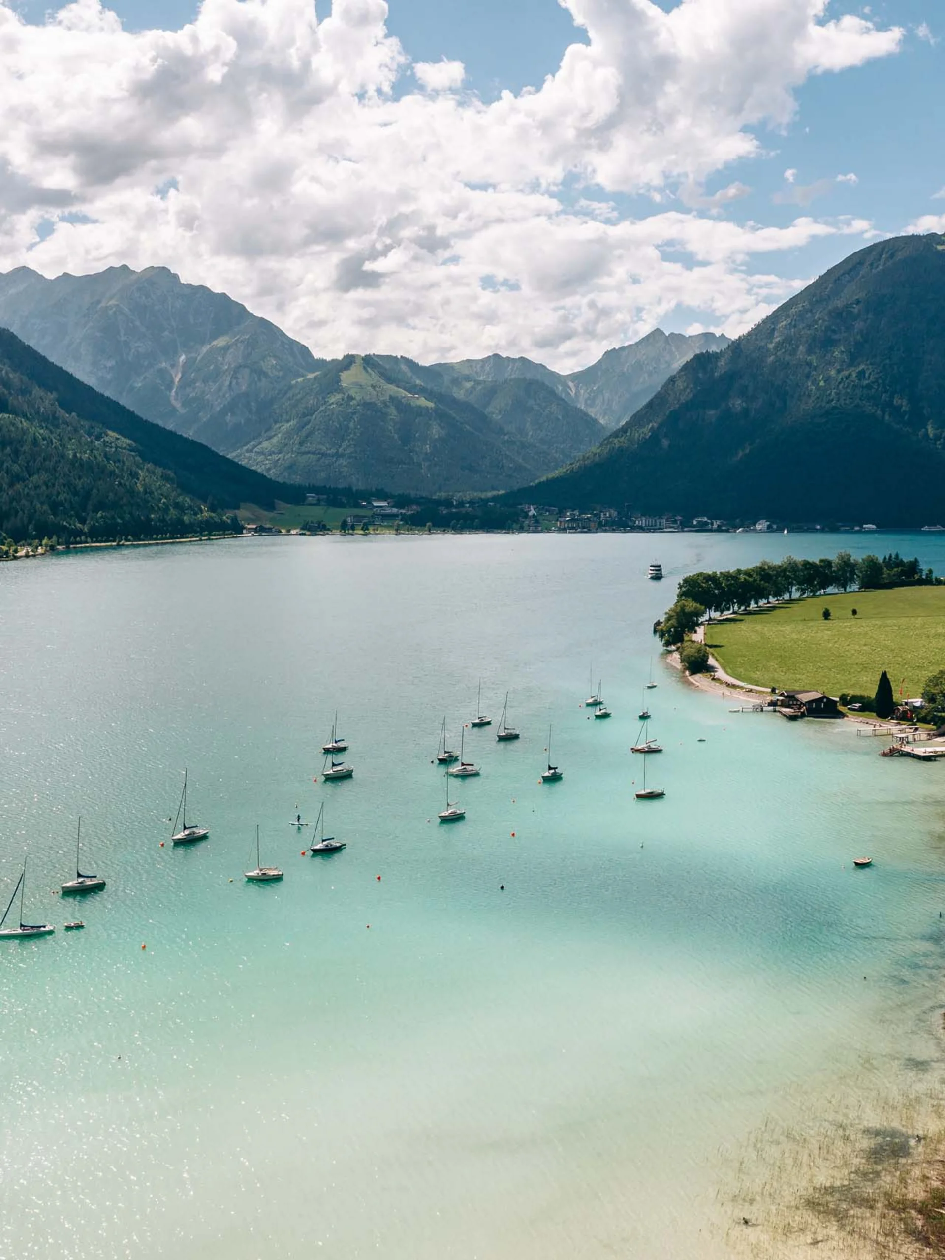 Wassersport auf dem See in Österreich Blick auf einen See mit Segelbooten und Bergen im Hintergrund bei sonnigem Himmel