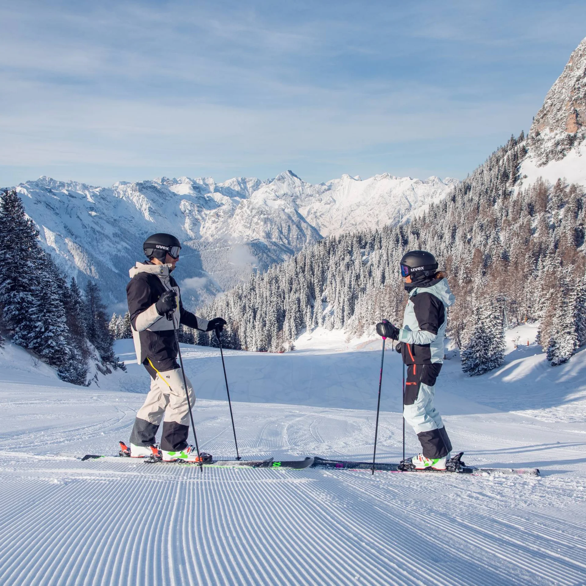 Der Wintertraum im Familien-Skihotel in Österreich Zwei Skifahrer auf einer präparierten Piste vor verschneiten Bergen und Bäumen