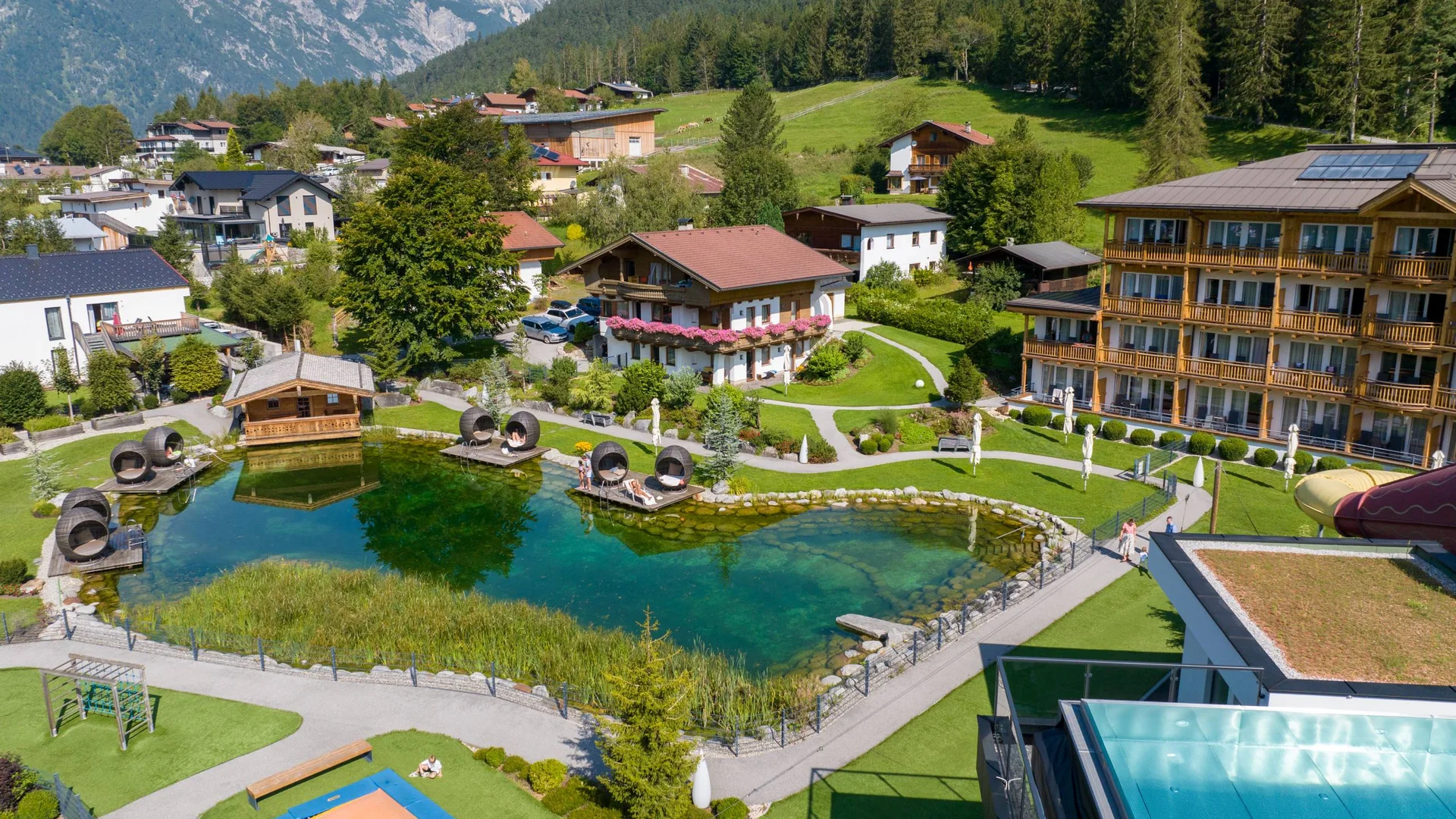 Urlaub im Wellnesshotel mit Kindern in Tirol Hotelanlage mit natürlichem Schwimmteich und Liegebereichen in den Bergen