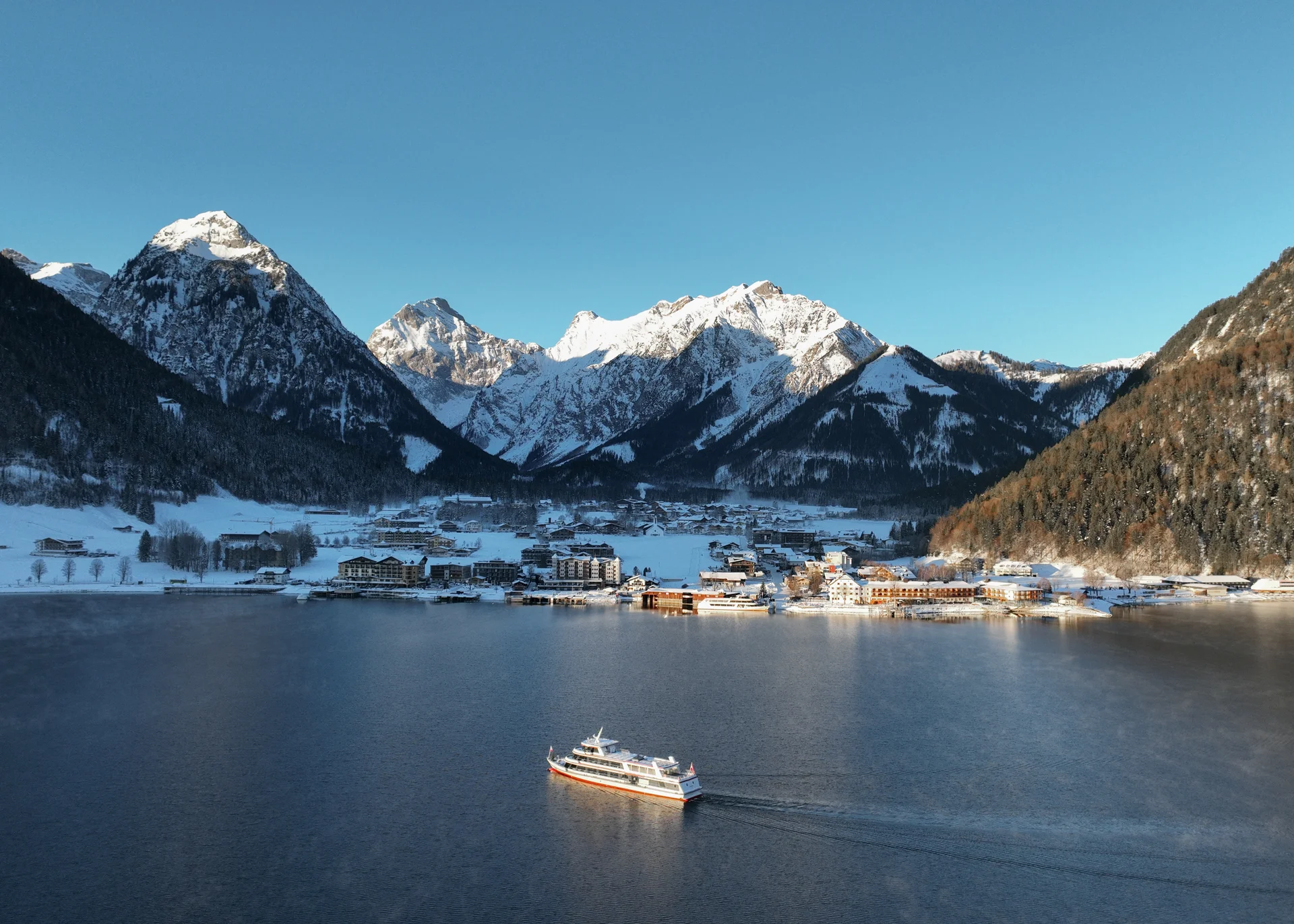 Willkommen im Familienhotel Buchau am Achensee Schiff auf See vor schneebedecktem Bergdorf in klarer Winterlandschaft
