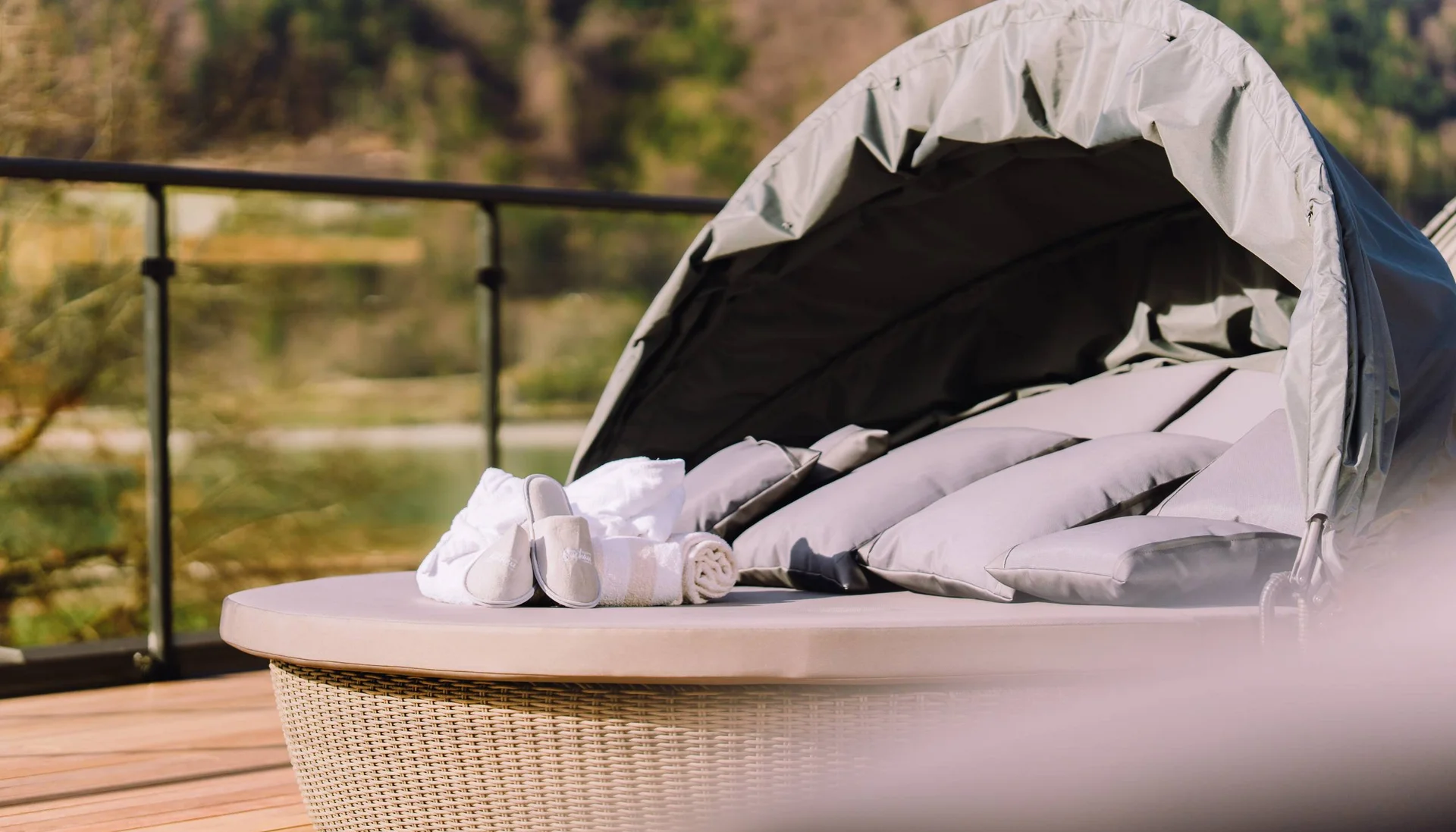 Ab ins Wellnesshotel in Tirol, in den Infinitypool! Rundes Loungesofa mit Kissen, Handtüchern und Hausschuhen auf Holzterrasse
