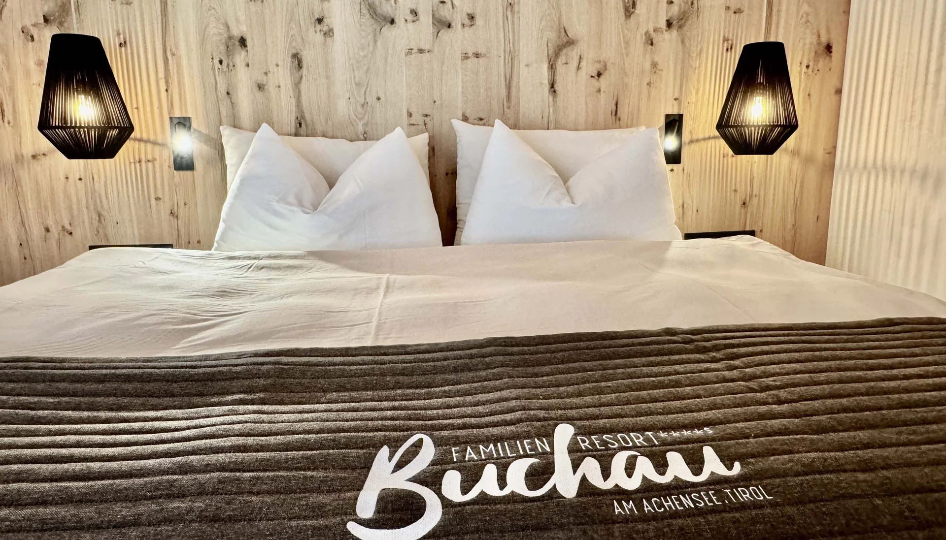 Zimmer und Angebote am Achensee Gemütliches Doppelbett mit Holzrückwand und Beleuchtung im Familienresort Buchau Tirol