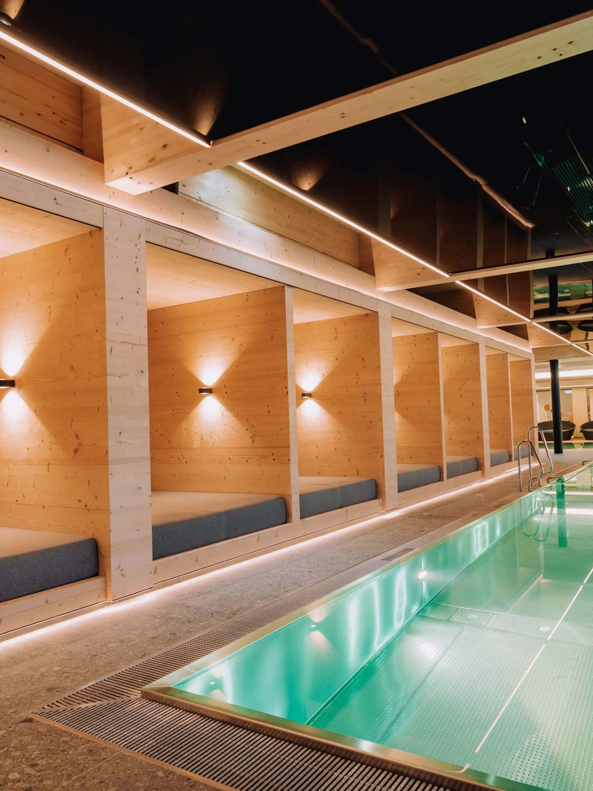 Wir lassen Bilder sprechen. Modernes Hallenbad mit Holzliegen und indirekter Beleuchtung