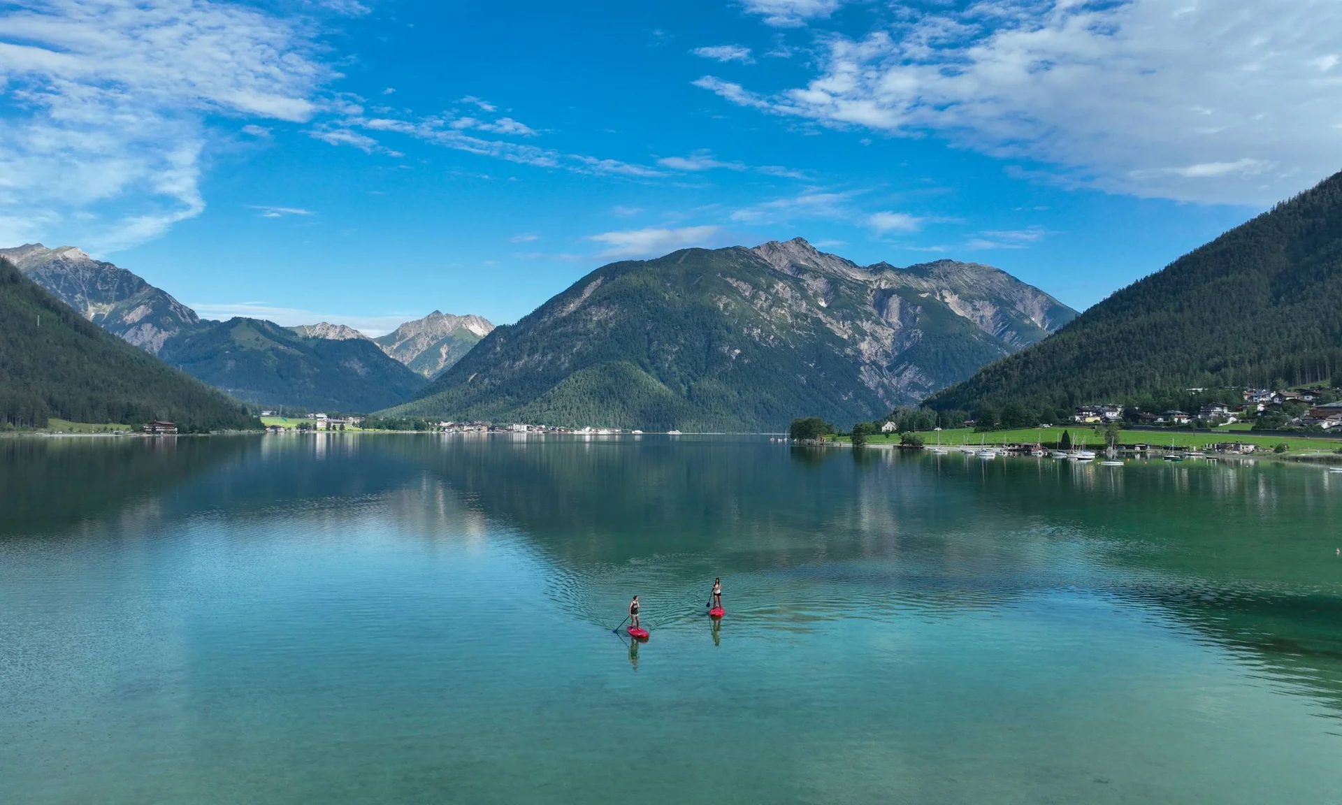 Wassersport auf dem See in Österreich Zwei Personen paddeln auf einem See mit Bergen und Dorf im Hintergrund