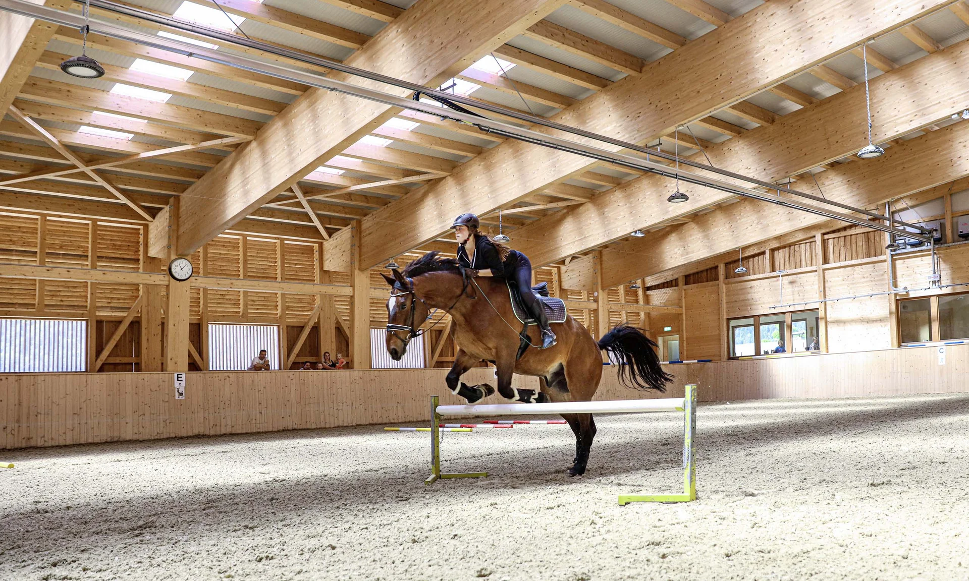 Urlaub im Hotel mit Indoorspielplatz Reiter springt mit Pferd in einer großen Reithalle über Hindernis