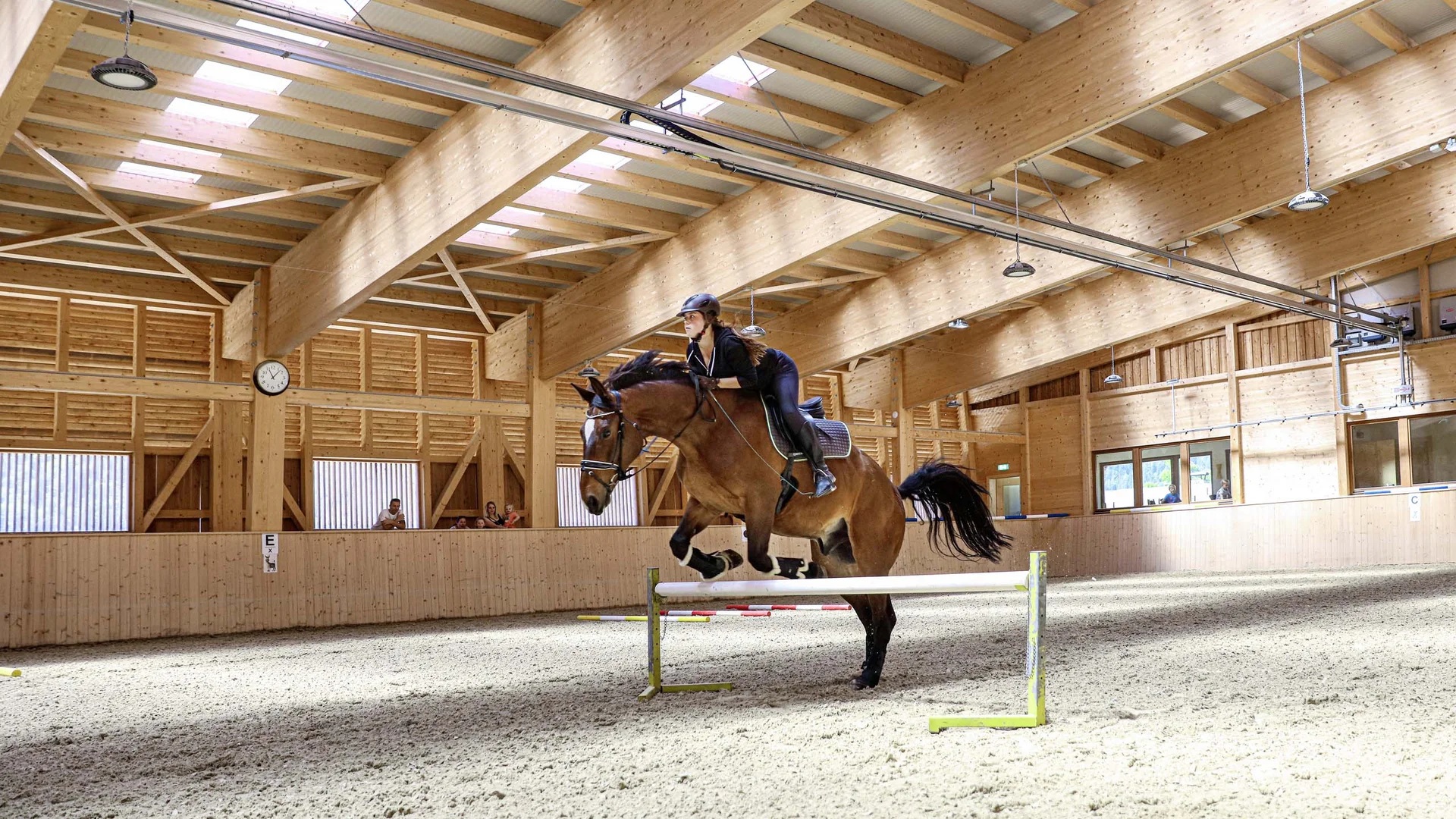 Ihr abenteuerlicher Erlebnisurlaub in Österreich Reiter springt mit Pferd in einer großen Reithalle über Hindernis