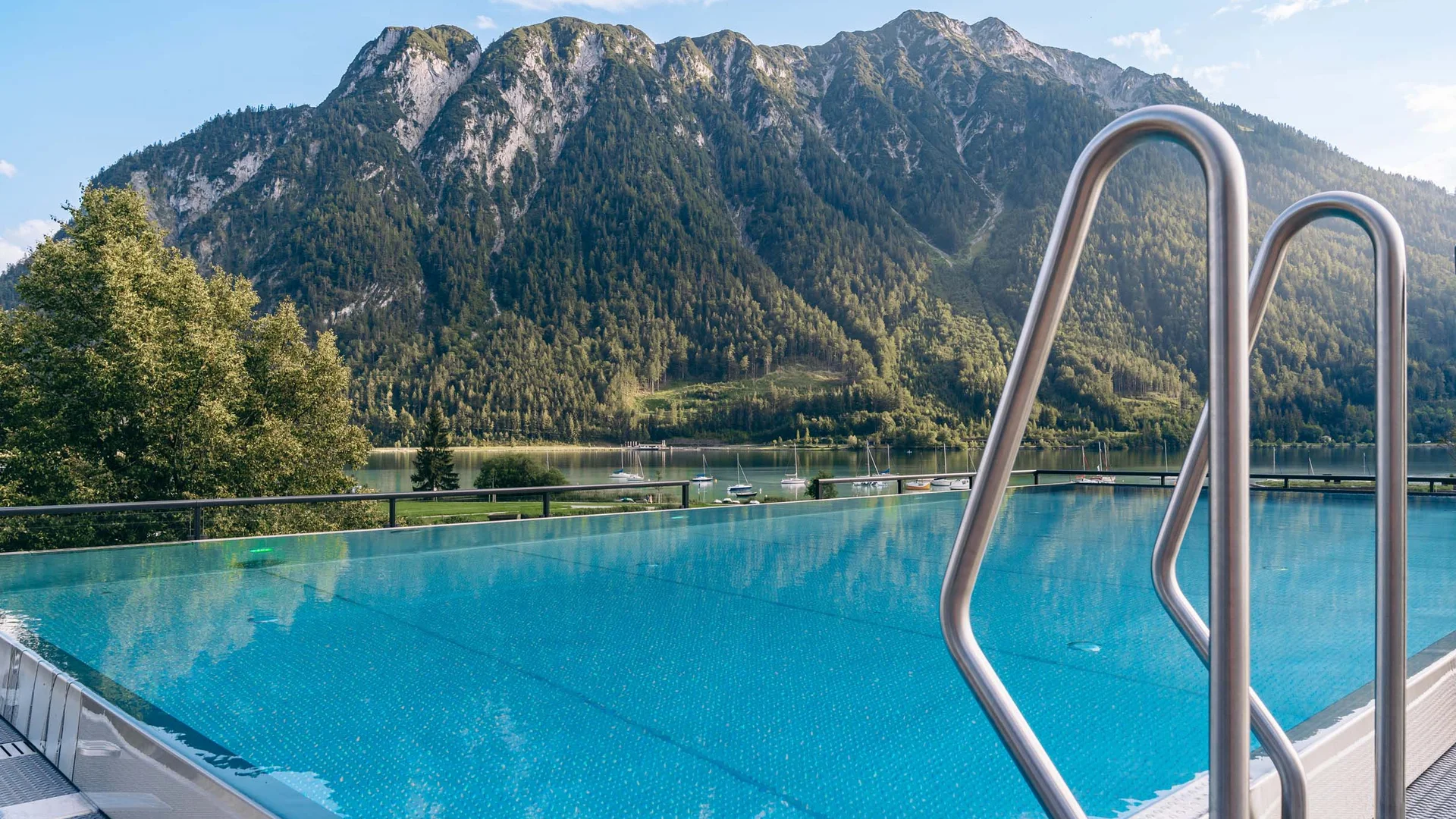 Welcome to our family hotel at Lake Achensee. Infinity pool with mountain and lake view under clear sky