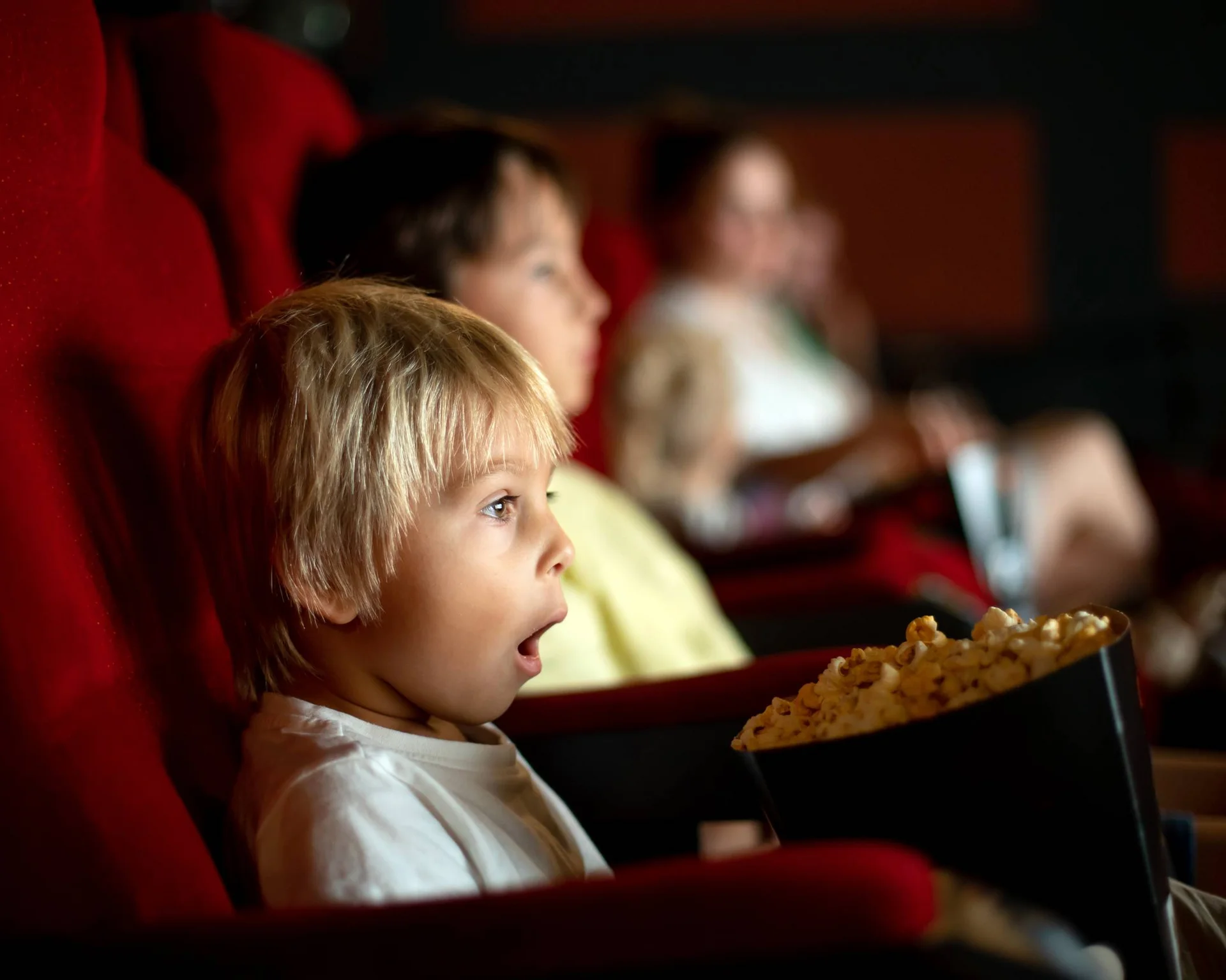 Urlaub im Hotel mit Indoorspielplatz Kind schaut überrascht im Kino sitzend mit Popcorn