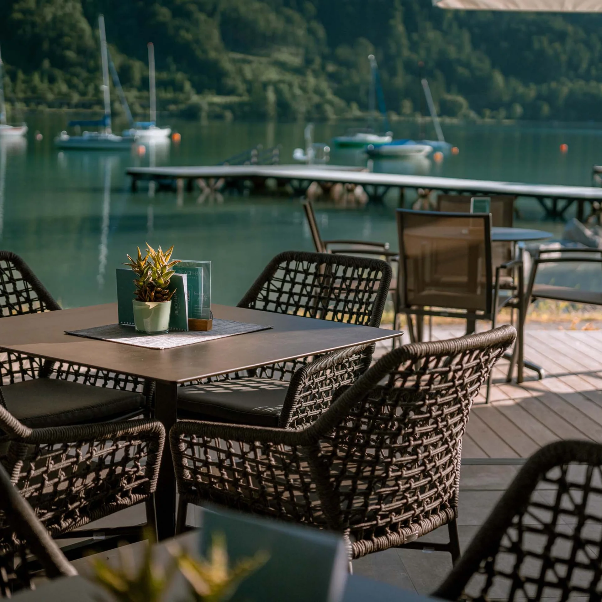 Familienurlaub mit Baby und Kleinkind im Buchau Leere Sitzplätze am Tisch einer Terrasse mit Blick auf See und Steg