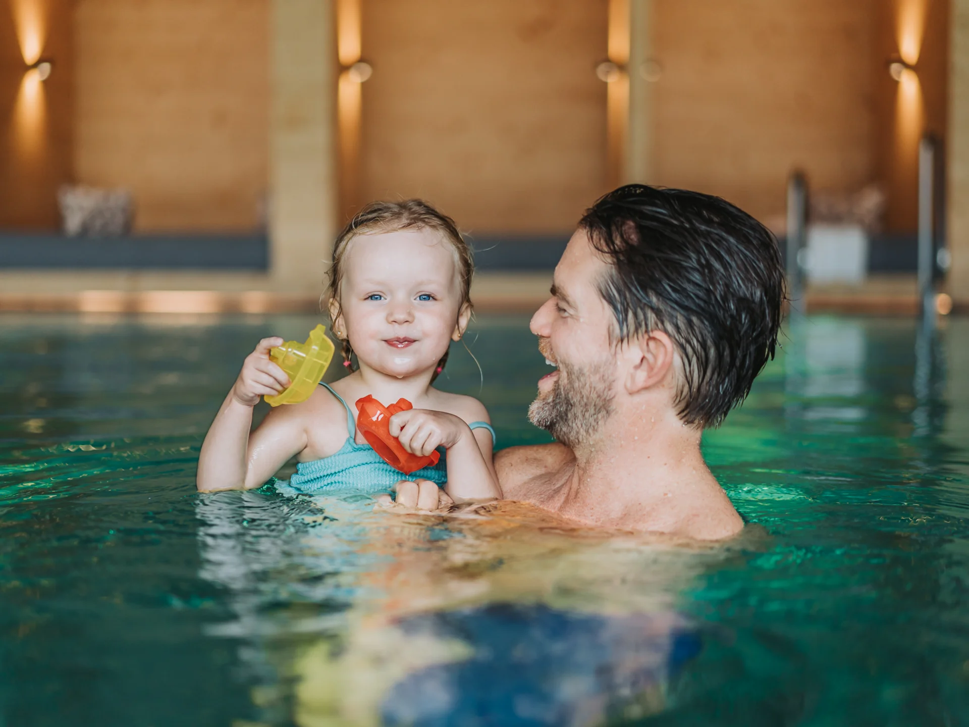 Ihr Hotel für Alleinerziehende Vater hält lachendes kleines Mädchen mit Spielzeugbooten im Hallenbad