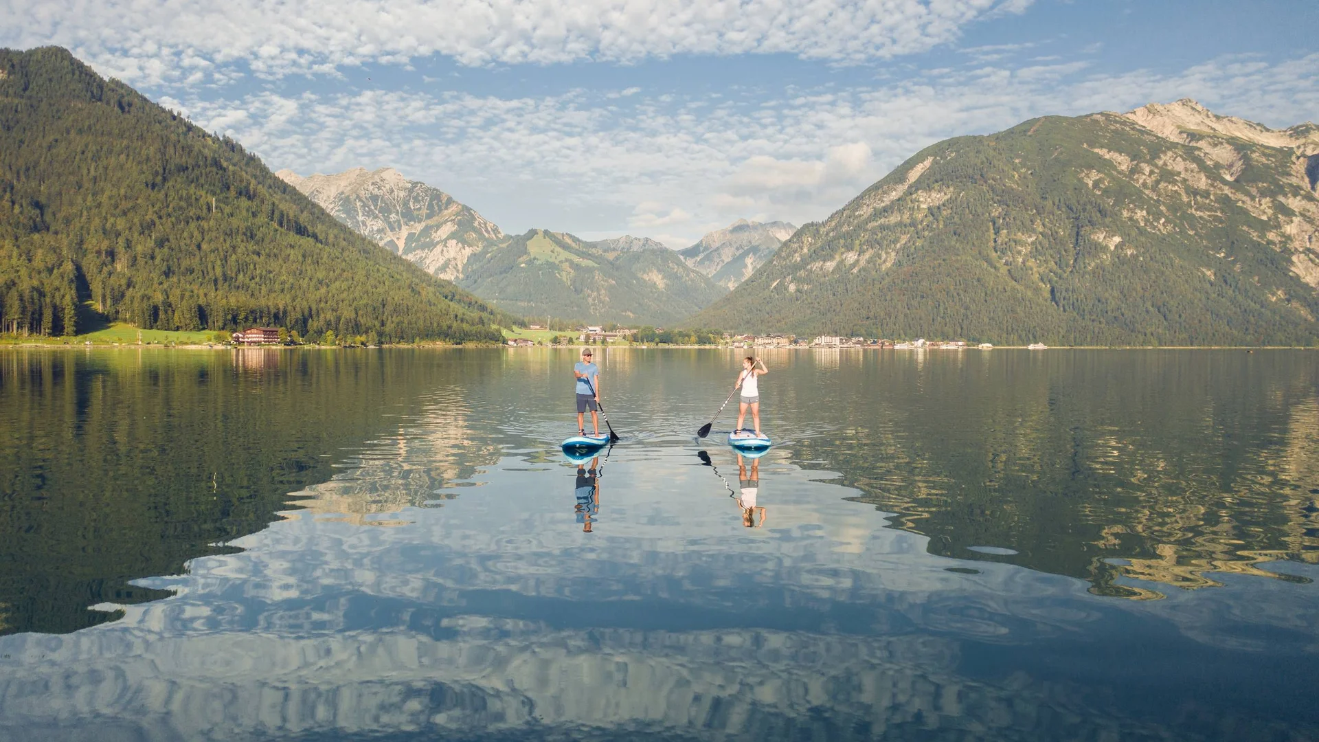 Wassersport auf dem See in Österreich Zwei Menschen beim Stand-up-Paddling auf einem Bergsee mit bewölktem Himmel