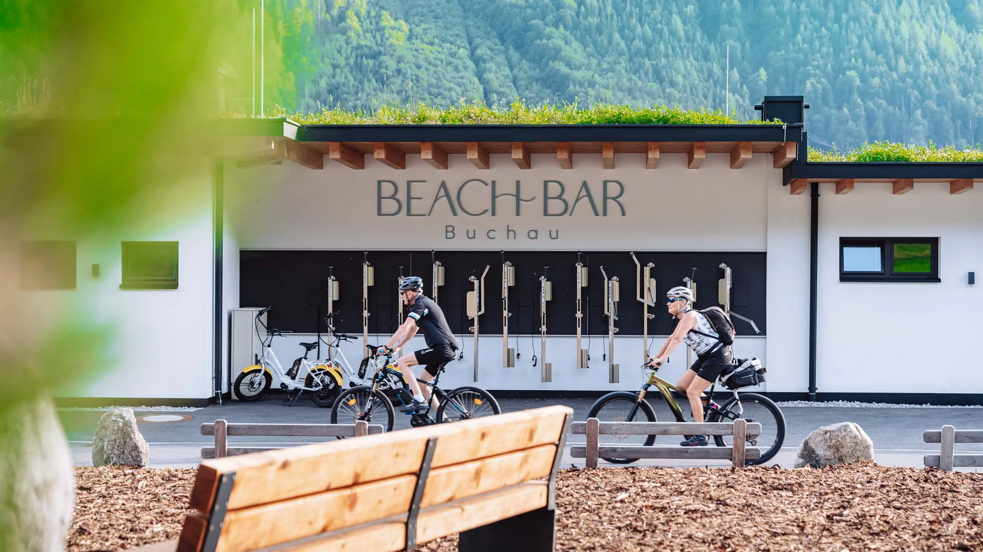 Vom Wanderhotel in Tirol direkt in die Natur Zwei Radfahrer vor der Beach Bar Buchau mit grünen Bergen im Hintergrund