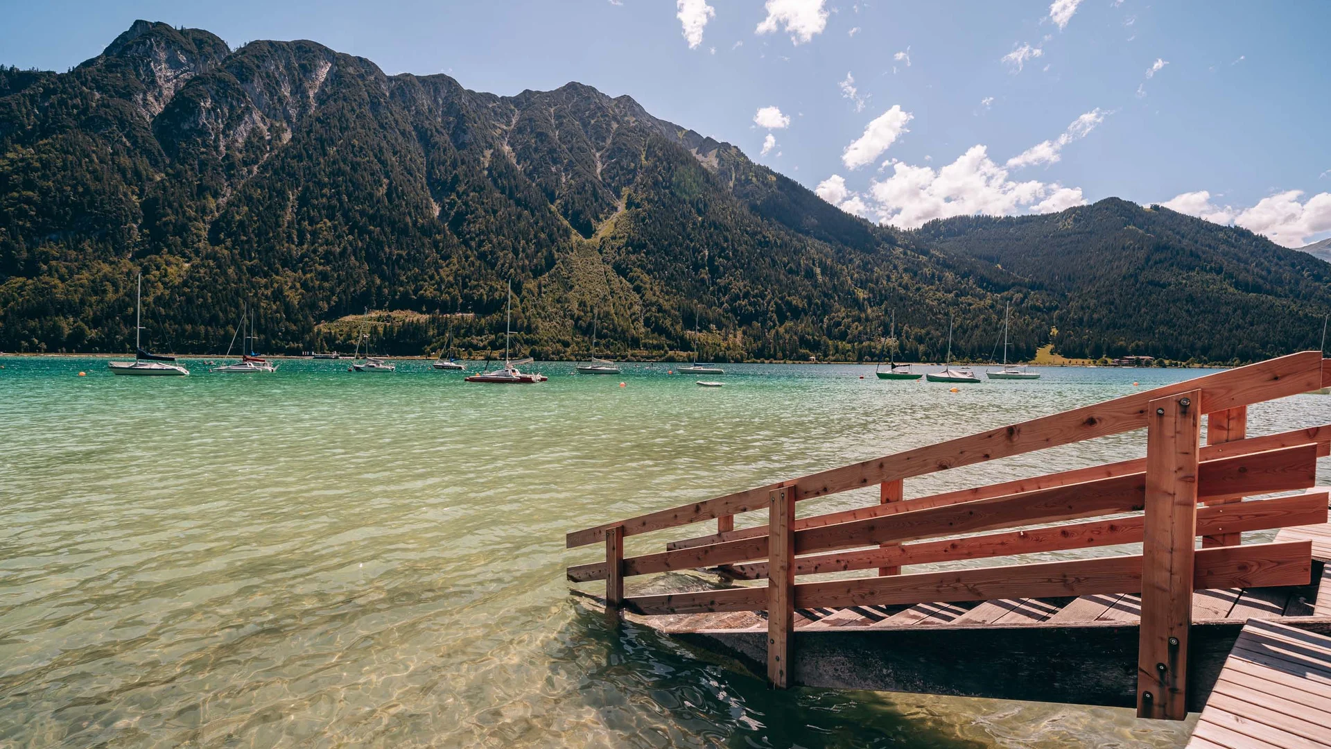 Wassersport auf dem See in Österreich Bergsee mit Holzsteg und Booten vor bewaldeten Bergen bei klarem Himmel