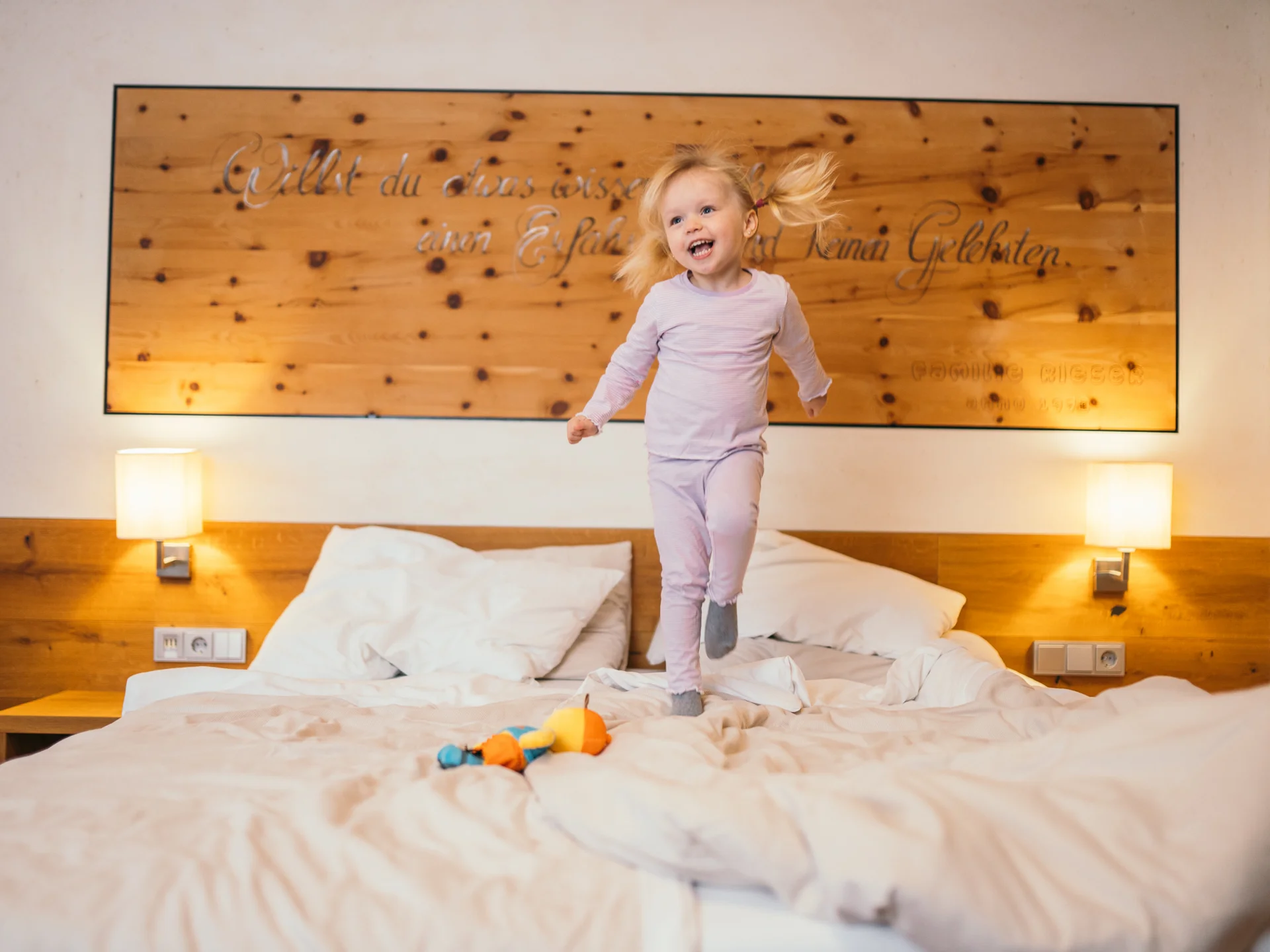 Welcome to our family hotel at Lake Achensee. Little girl in pajamas jumping happily on a bed in a bedroom