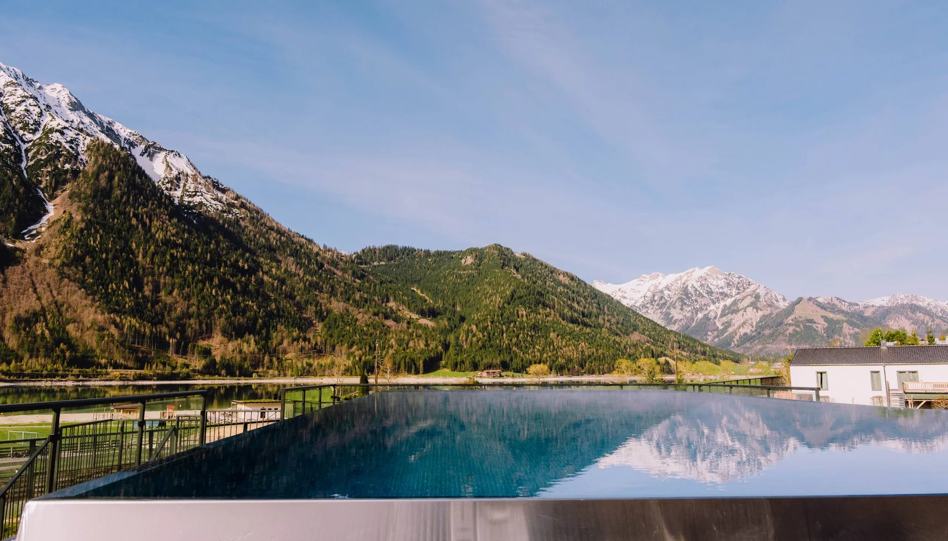 Ab ins Wellnesshotel in Tirol, in den Infinitypool! Infinity-Pool mit Bergblick und Spiegelung bei klarem Himmel