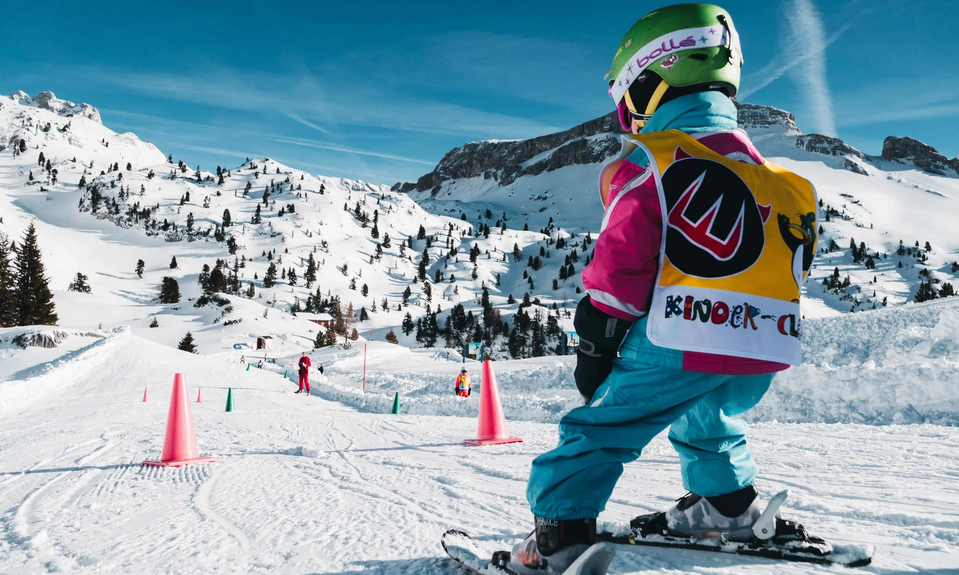 Freizeitkurse für Ihre Kids und Teenies Kind fährt Ski auf verschneiter Piste mit bunten Hütchen und Bergen im Hintergrund
