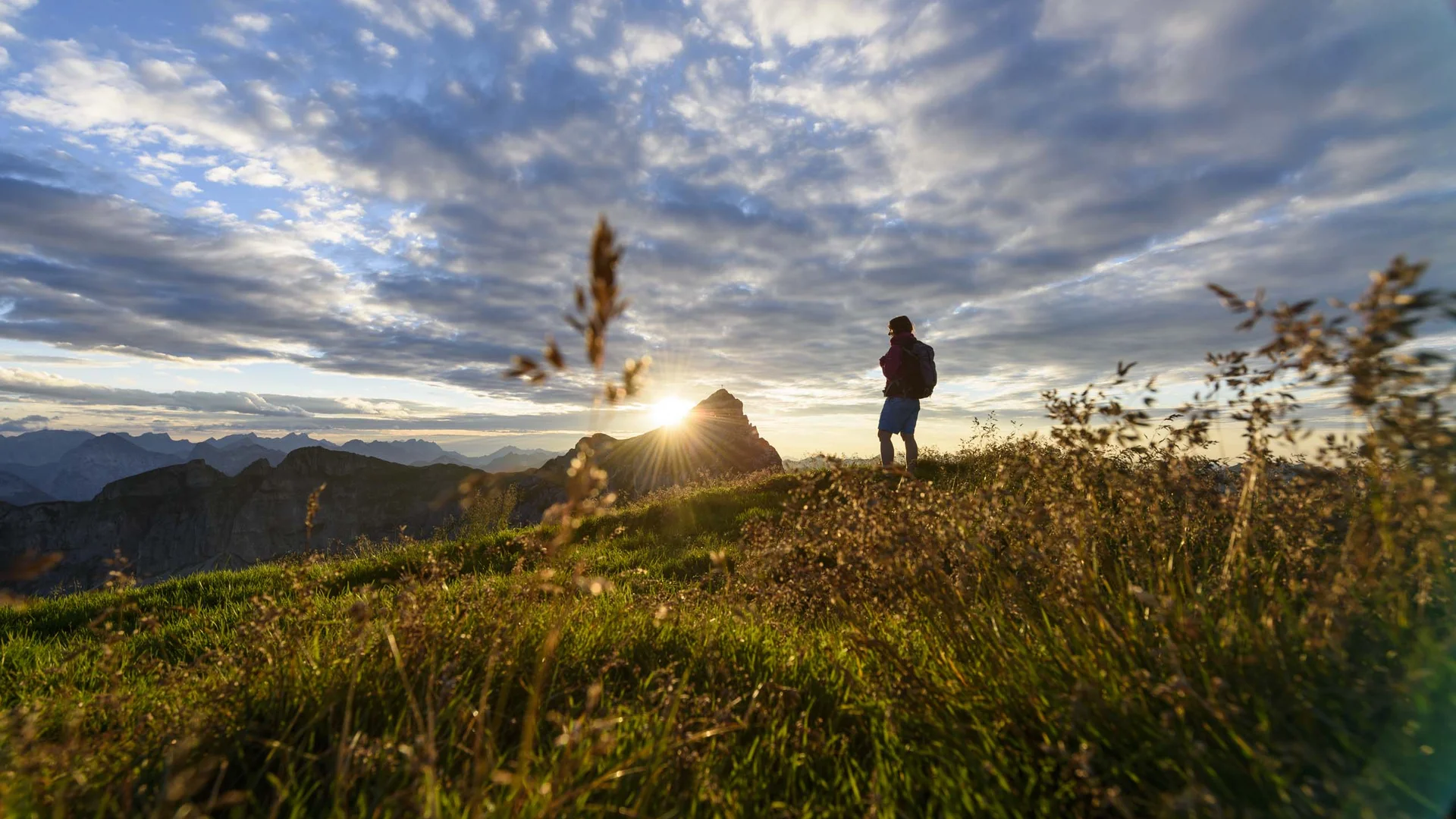 Vom Wanderhotel in Tirol direkt in die Natur Wanderer steht auf Berg mit Sonnenuntergang und dramatischem Himmel