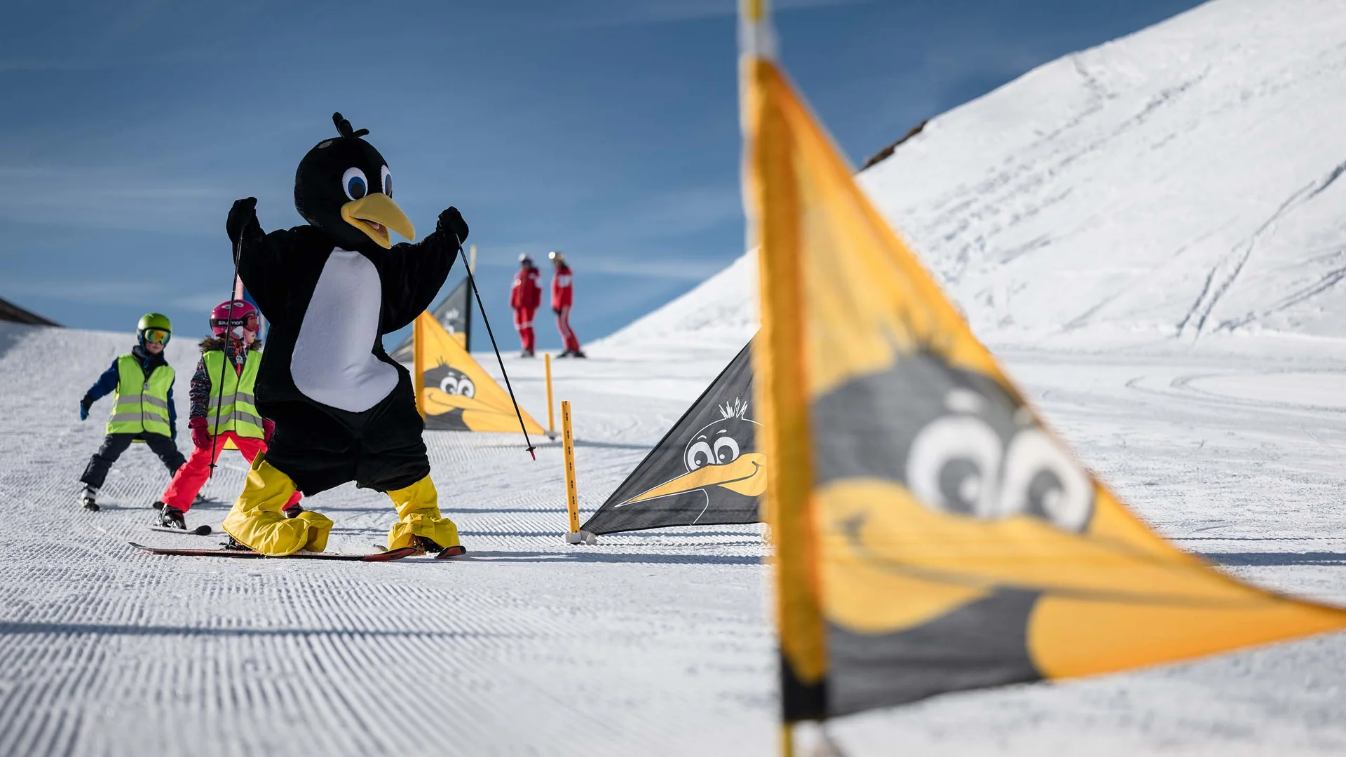Der Wintertraum im Familien-Skihotel in Österreich Person im Pinguinkostüm und Kinder beim Skifahren im Schnee