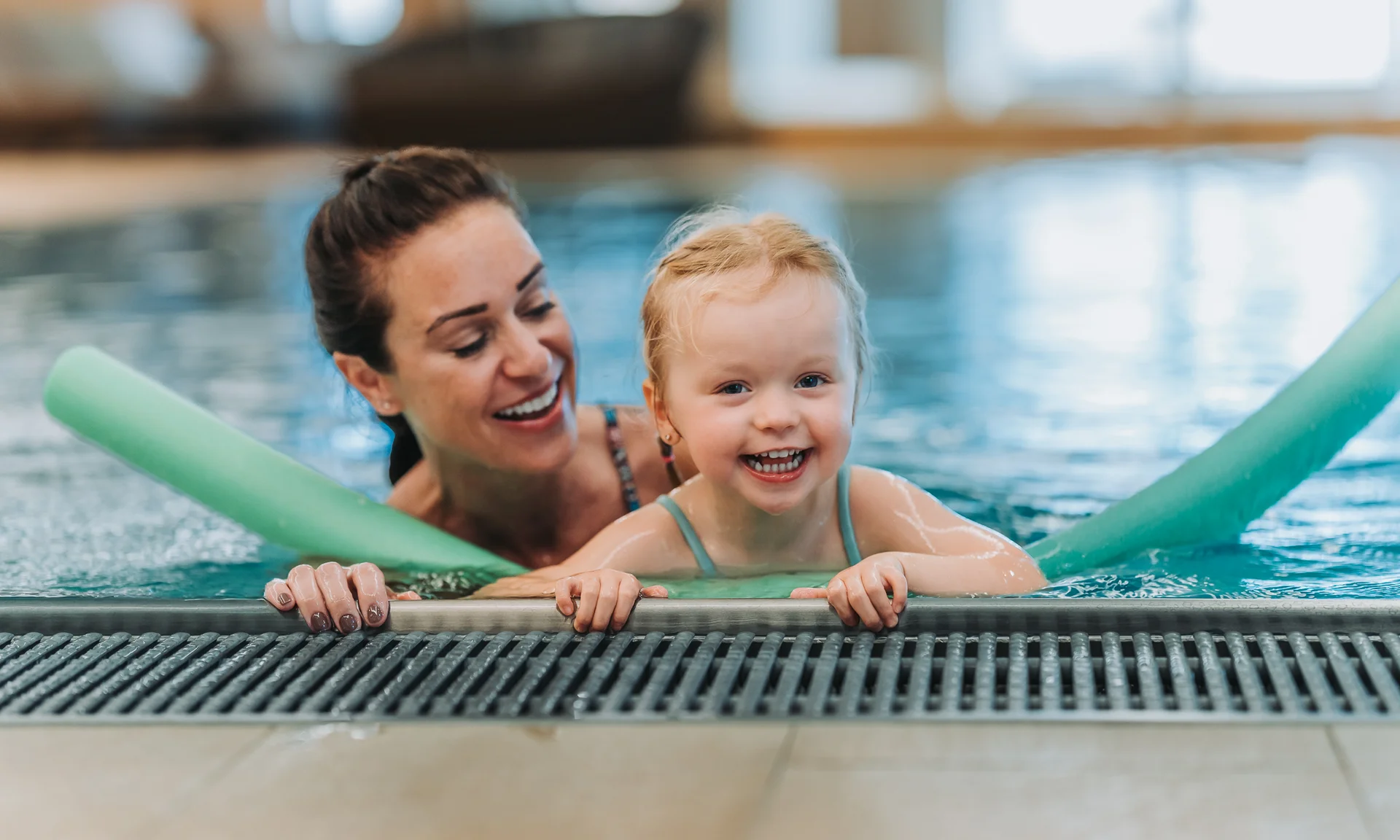 Wir lassen Bilder sprechen. Glückliches Kind mit Schwimmnudeln lernt im Schwimmbad mit Frau schwimmen