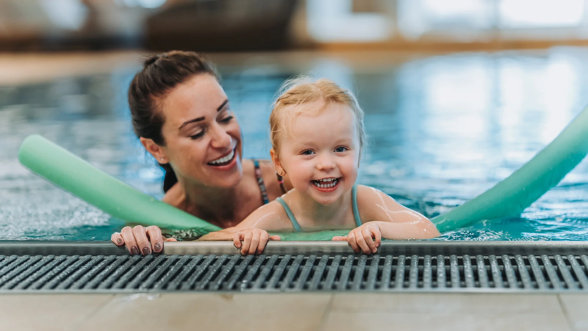 Wasserspaß im Familienhotel in Tirol mit Pool Glückliches Kind mit Schwimmnudeln lernt im Schwimmbad mit Frau schwimmen