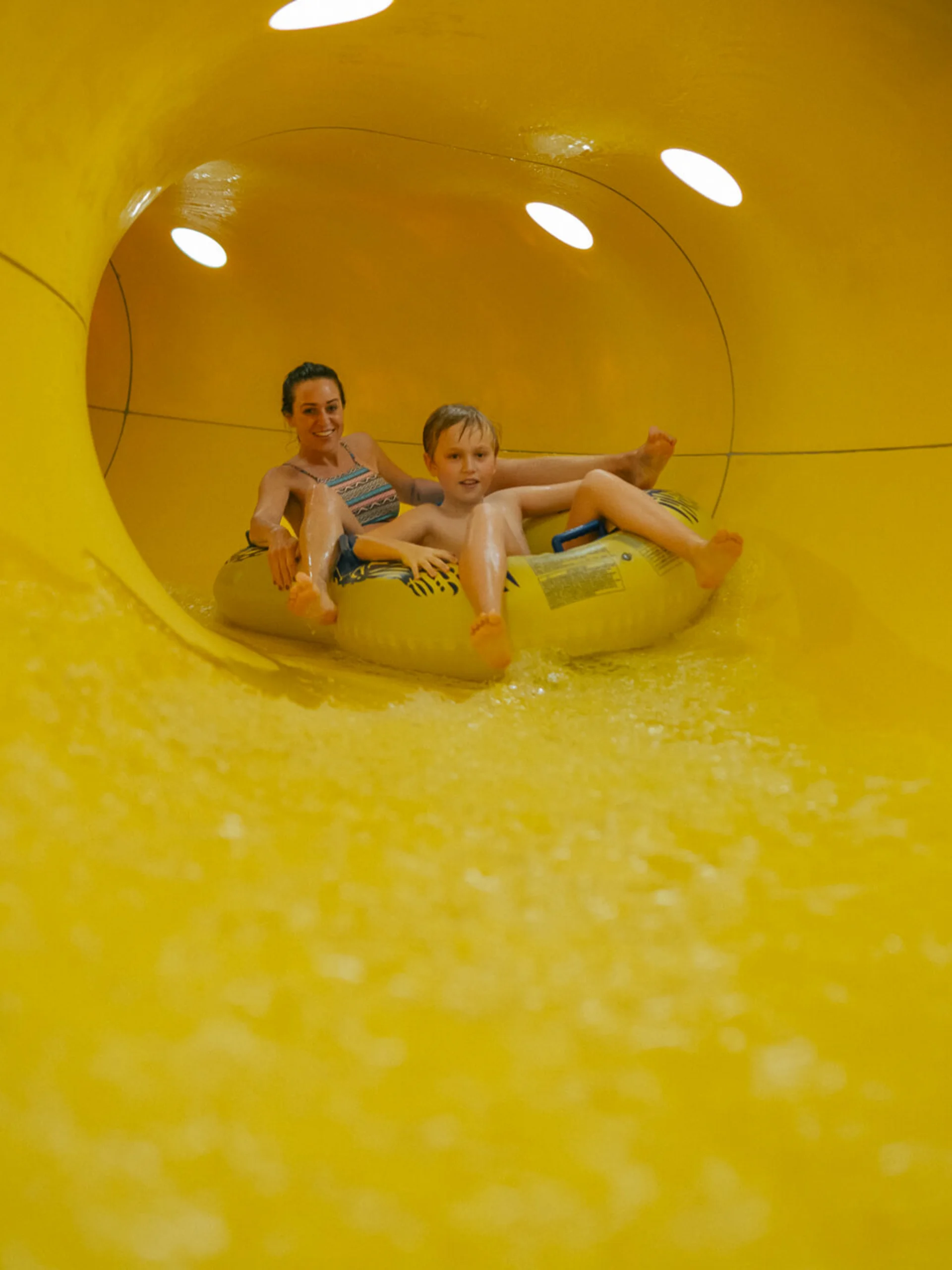 Wir lassen Bilder sprechen. Mutter und Sohn fahren gemeinsam auf einem Schlauchreifen in einer gelben Wasserrutsche