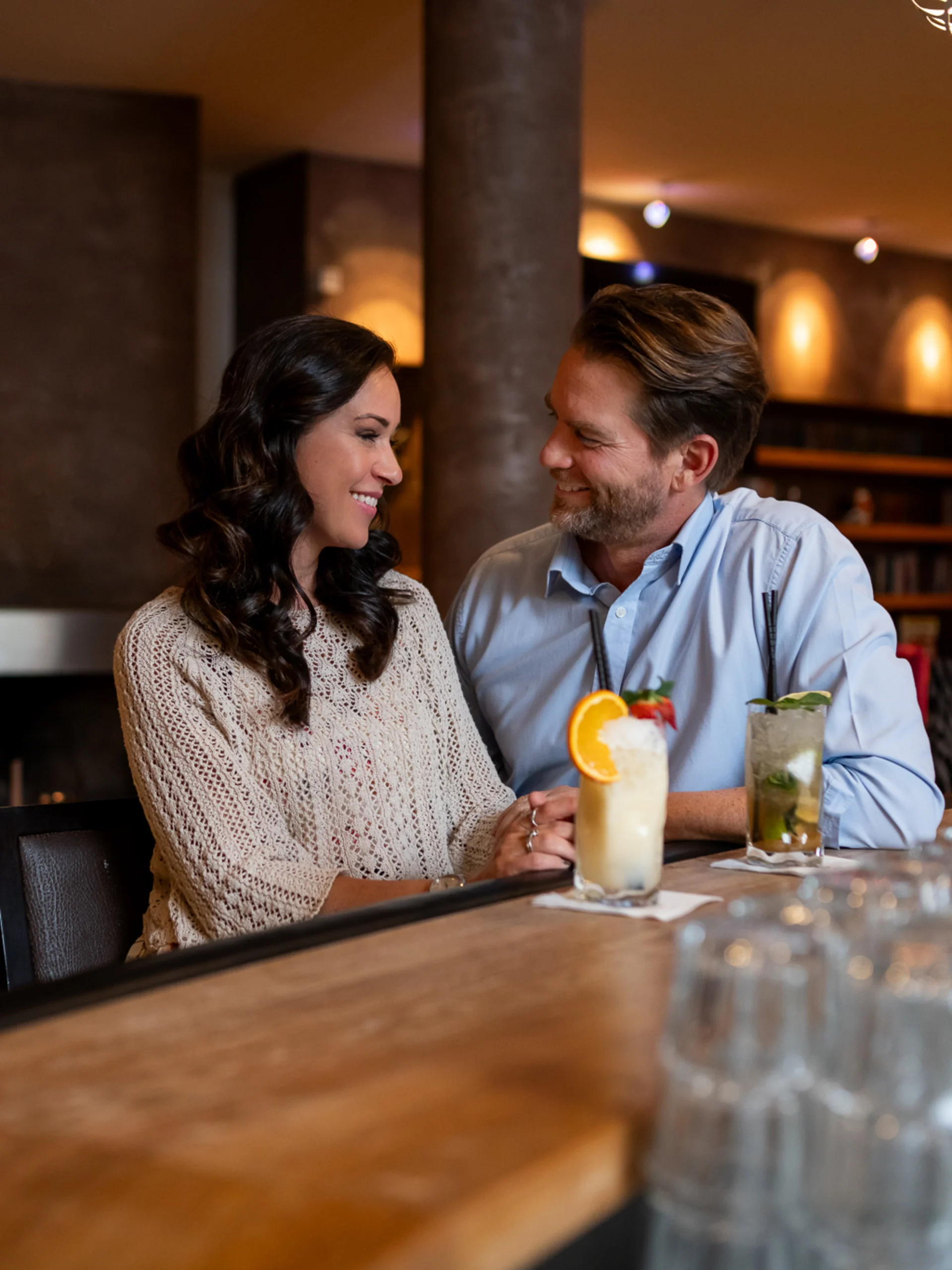 Welcome to our family hotel at Lake Achensee. Couple sitting at bar with cocktails in cozy bar with fireplace in background