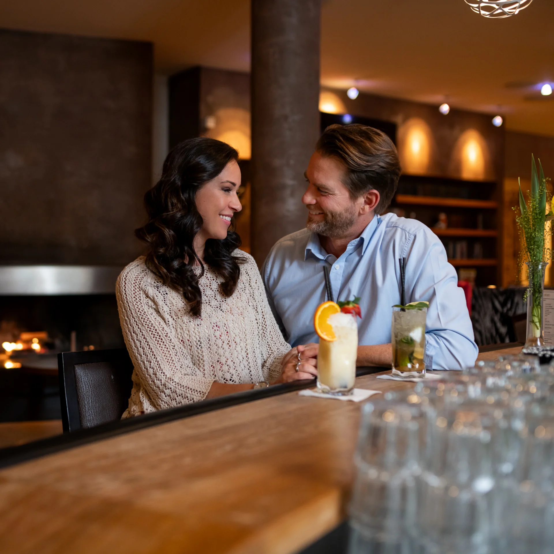 Familienzeit im Kinderhotel Buchau am Achensee Paar sitzt an Bar mit Cocktails in gemütlicher Bar mit Kamin im Hintergrund