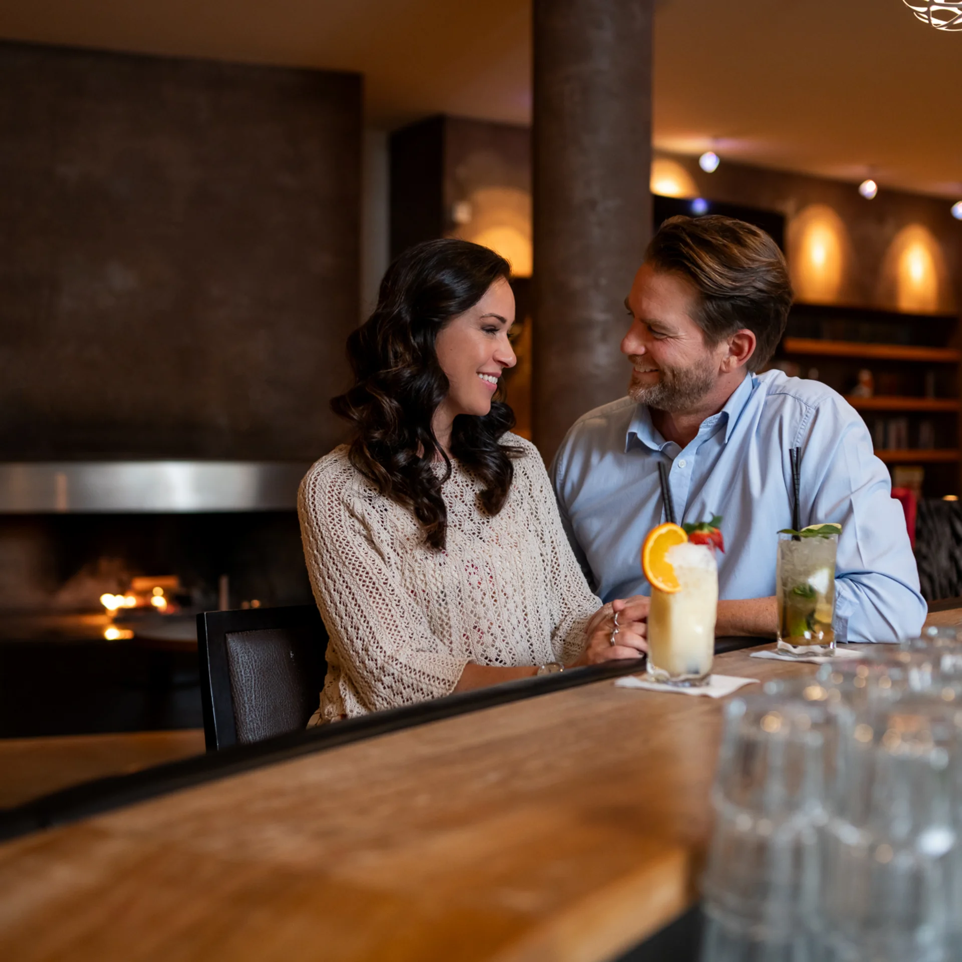 Welcome to our family hotel at Lake Achensee. Couple sitting at bar with cocktails in cozy bar with fireplace in background