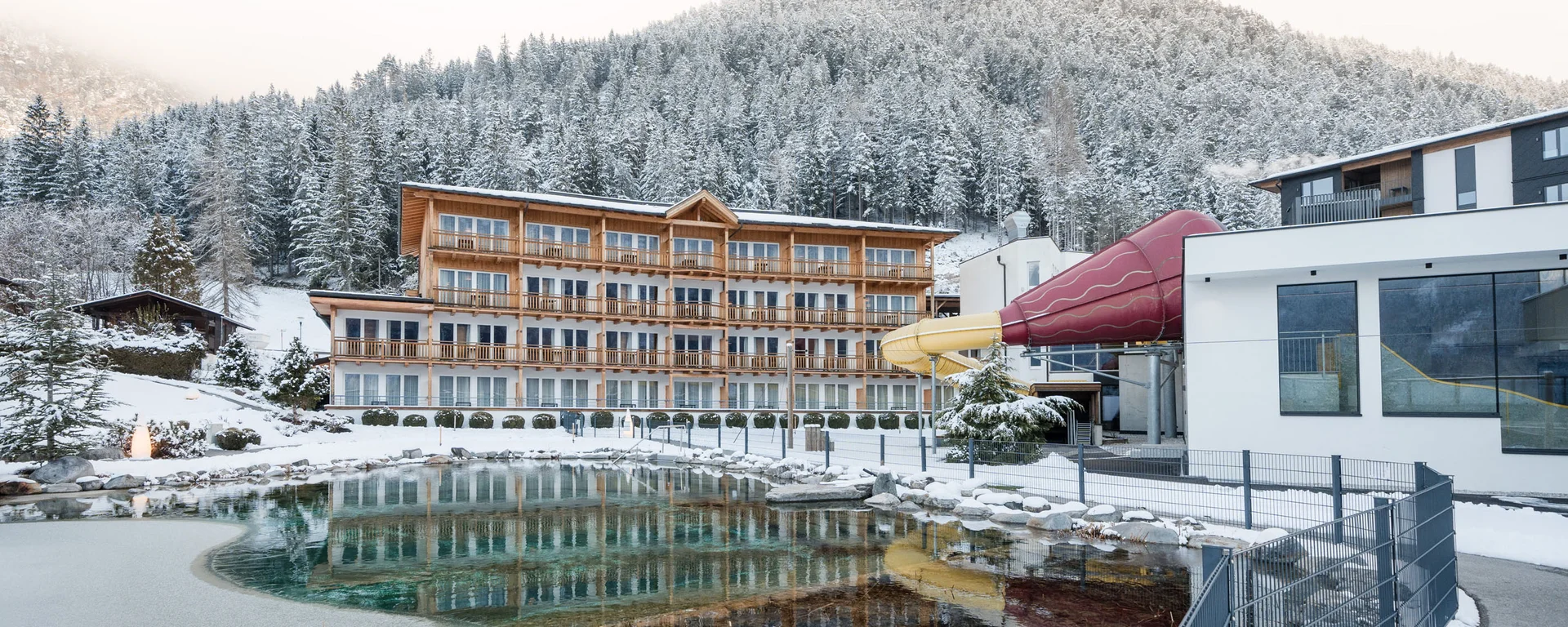 Familienzeit im Kinderhotel Buchau am Achensee Hotel mit Rutsche und Teich vor verschneitem Berg im Winter