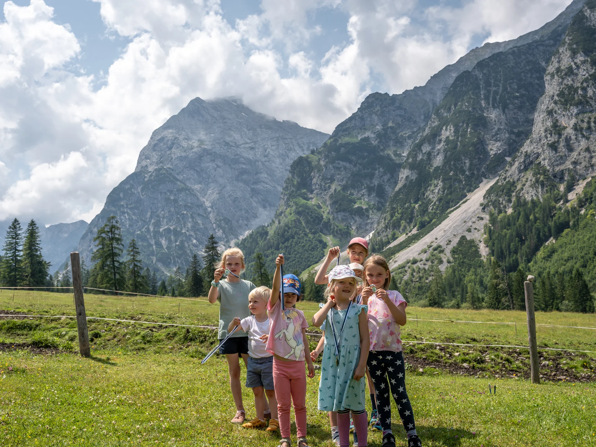Entspannte Ferien für die ganze Familie. Sieben Kinder zeigen im Bergwiesenfeld Auszeichnungen vor beeindruckenden Bergen