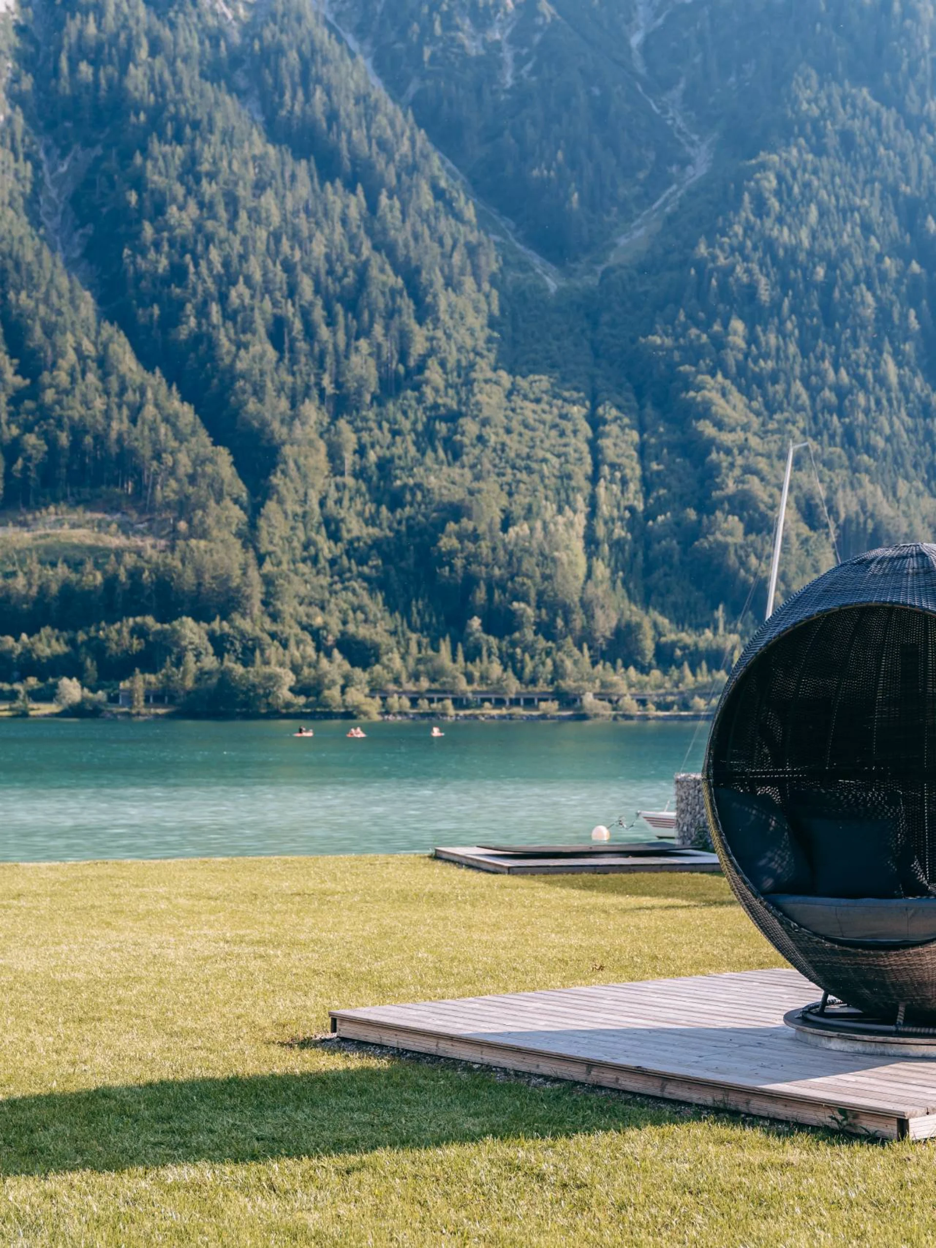 Wir lassen Bilder sprechen. Kugelsessel auf Holzplattform mit Bergsee und bewaldeten Bergen im Hintergrund