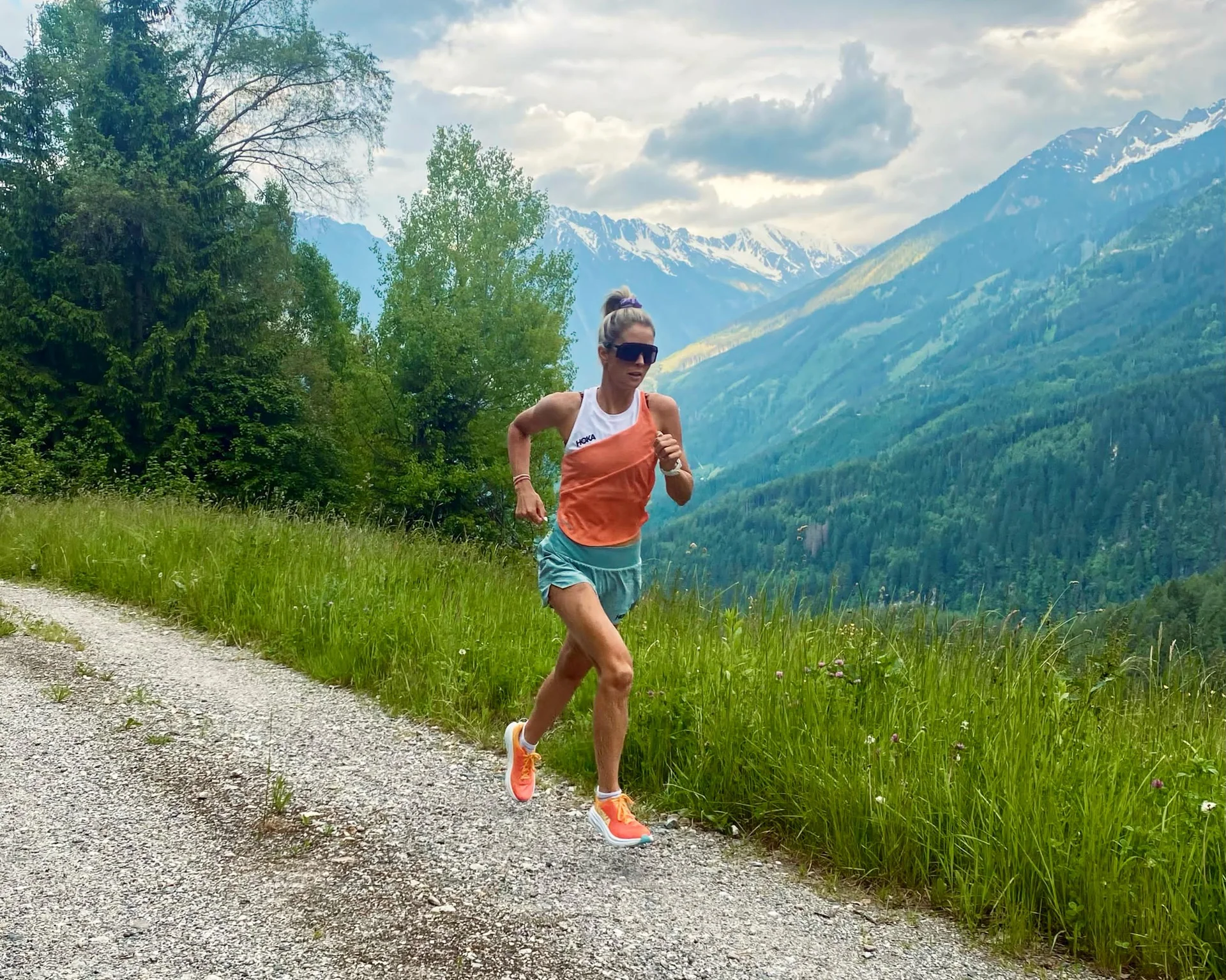 Willkommen im Familienhotel Buchau am Achensee Frau läuft auf einem Bergweg mit grünen Bäumen und schneebedeckten Bergen im Hintergrund