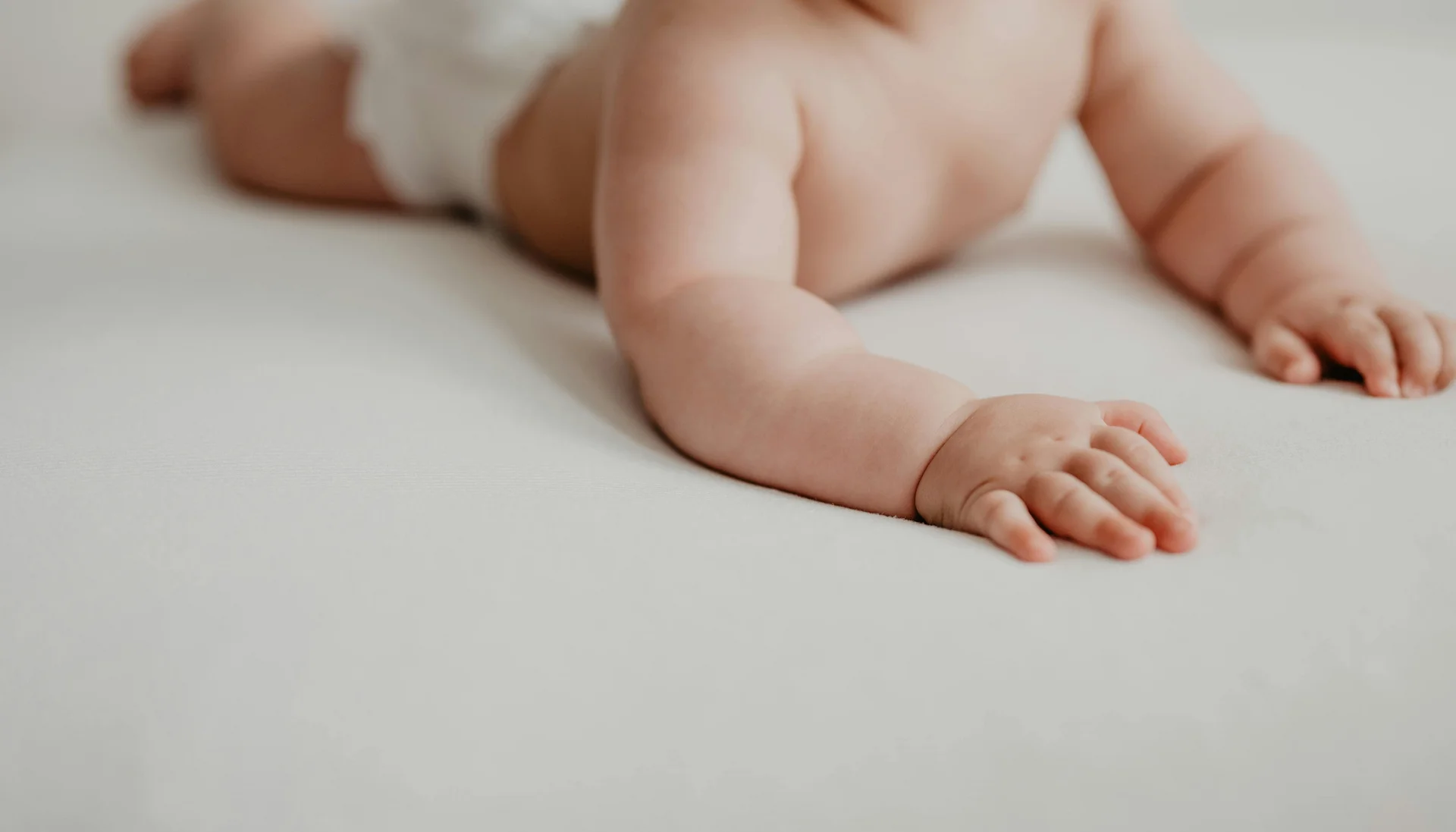 Familienurlaub mit Baby und Kleinkind im Buchau Baby krabbelt auf einer weißen Oberfläche, nur Oberkörper und Arme sichtbar