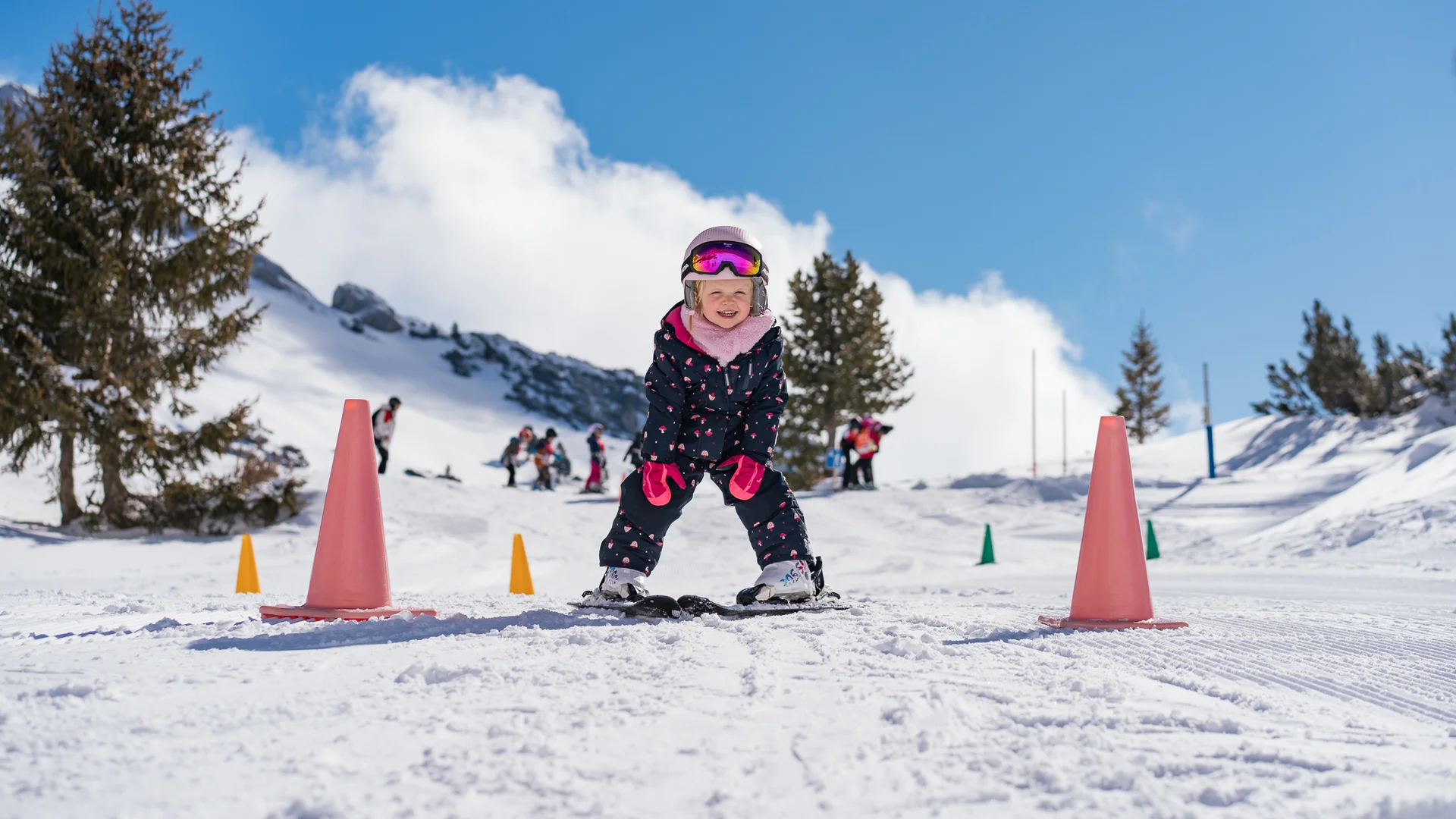 Der Wintertraum im Familien-Skihotel in Österreich Kleines Kind lernt Skifahren zwischen orangen Hütchen im Schnee bei Sonnenschein