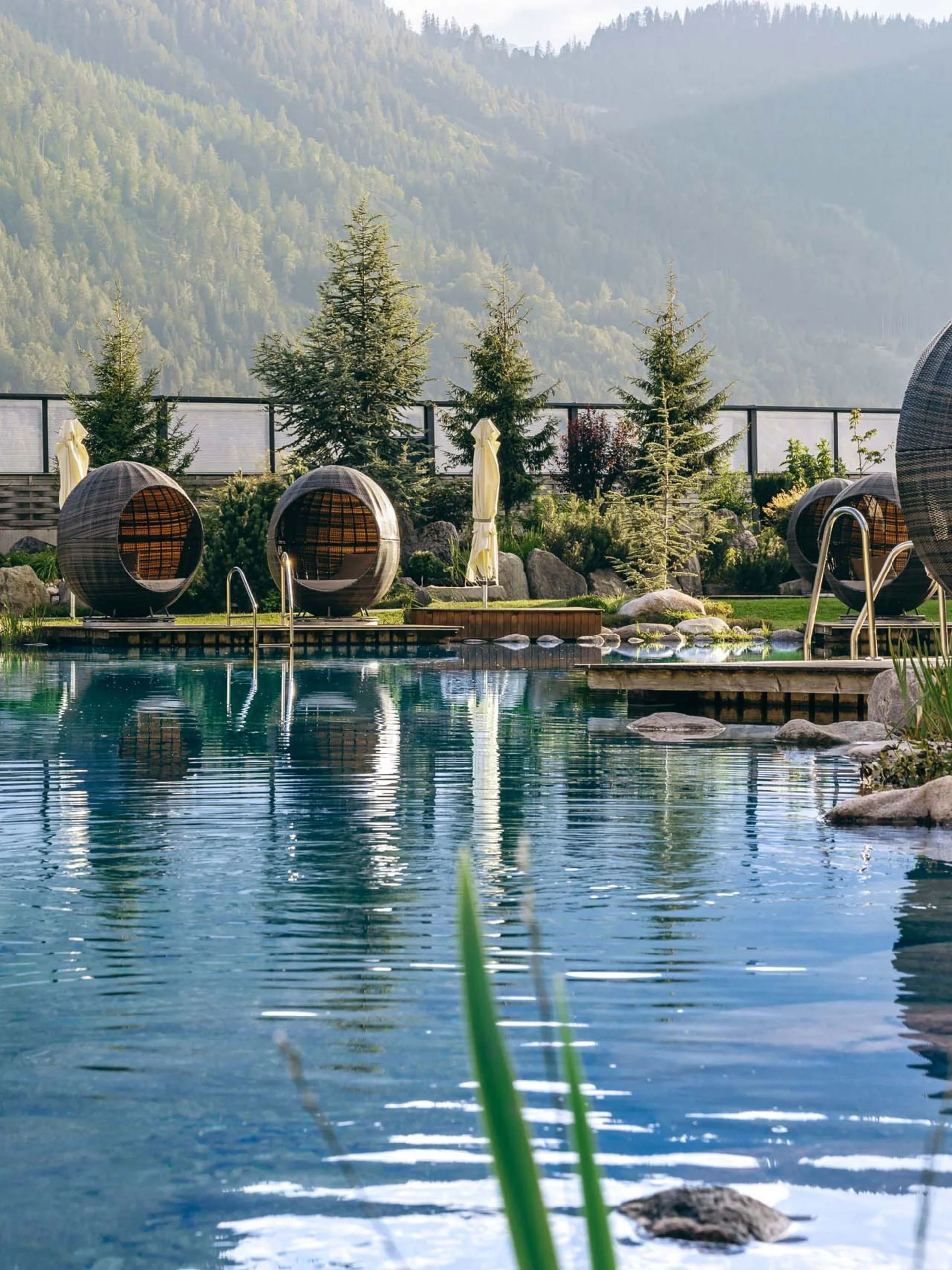 Wir lassen Bilder sprechen. Natürlicher Pool mit runden Lounge-Eiern und Bergen im Hintergrund