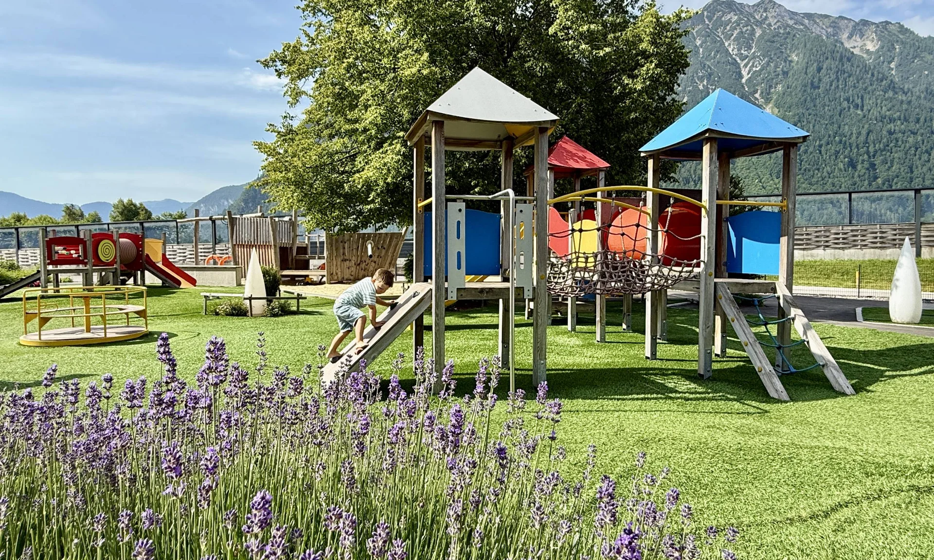 Welcome to our family hotel at Lake Achensee. Child climbing on colorful playground equipment with mountains in background