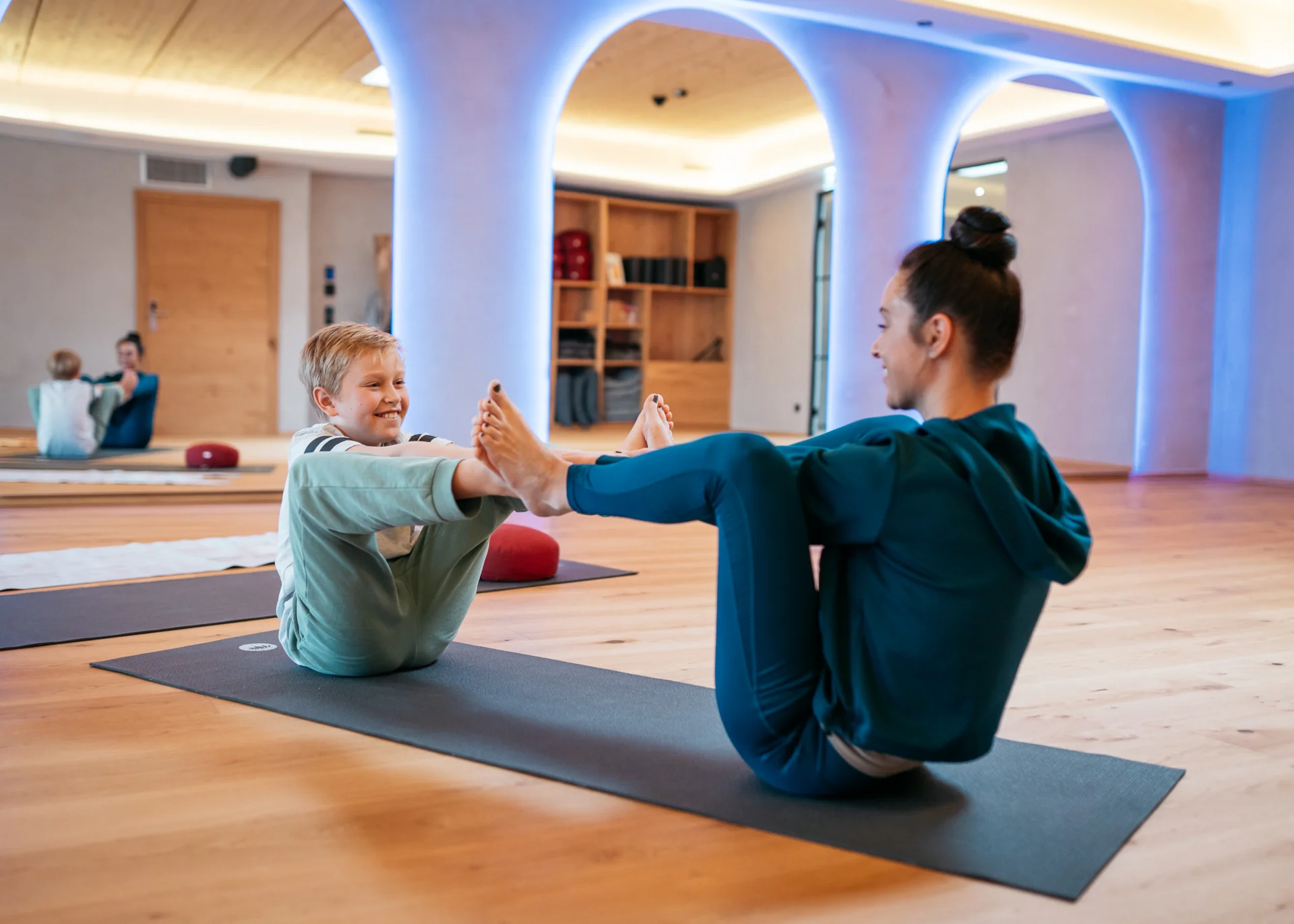 Fitness und Yoga im Hotel in Tirol Frau und Kind machen gemeinsam Yogaübungen auf Matten in einem Raum