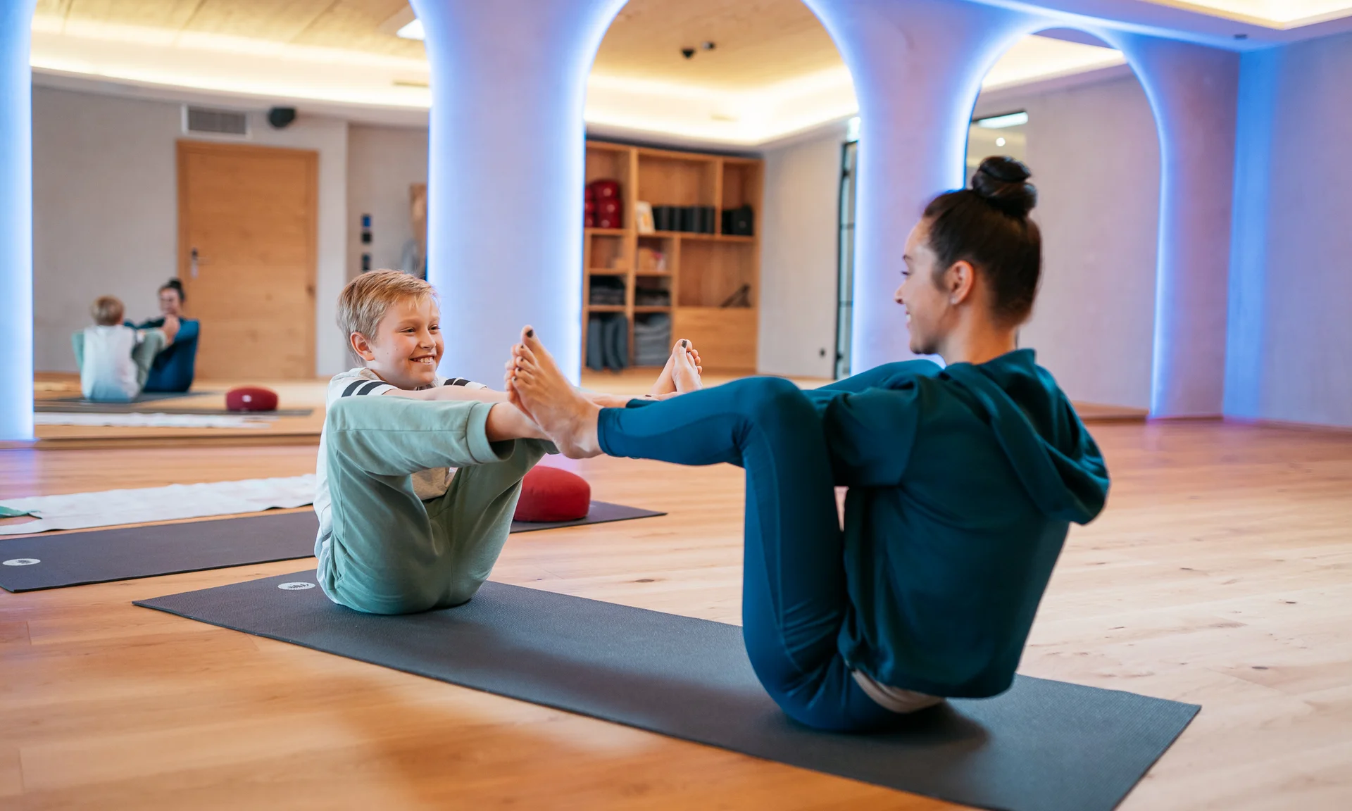Wir lassen Bilder sprechen. Frau und Kind machen gemeinsam Yogaübungen auf Matten in einem Raum