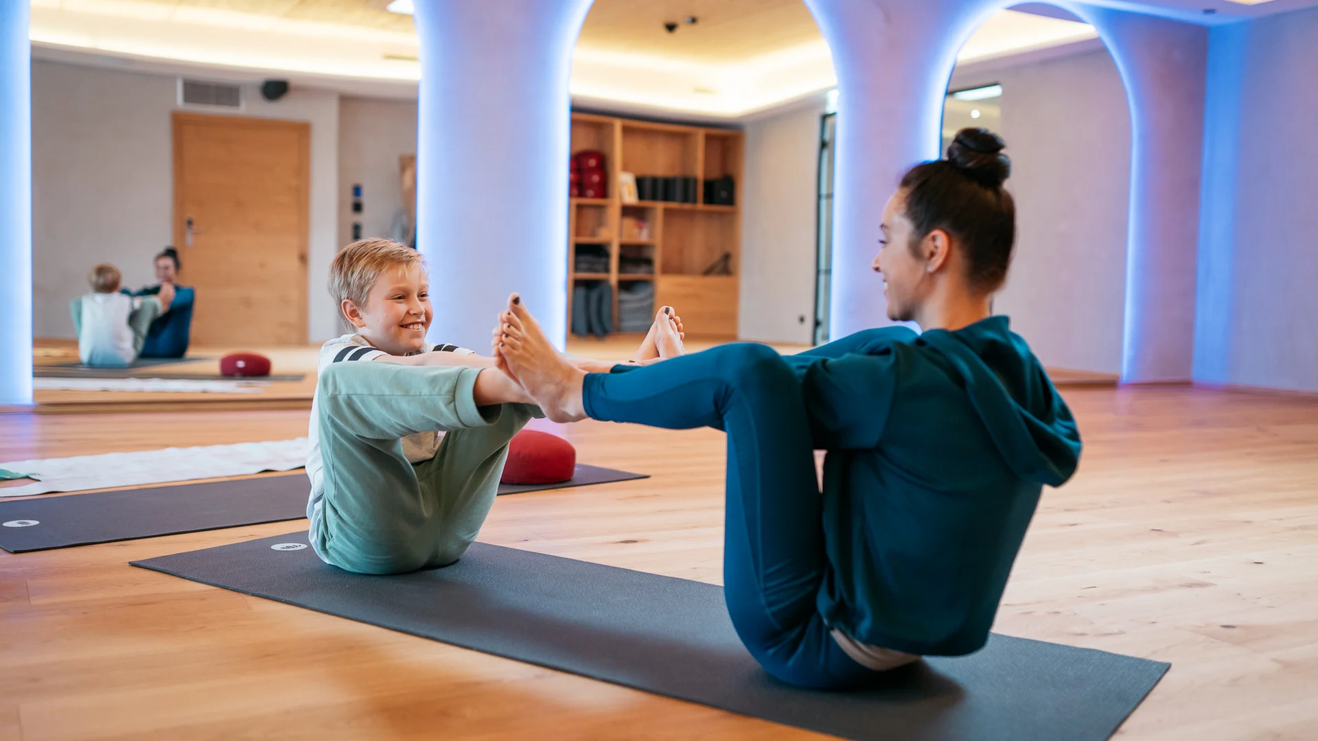 Urlaub im Wellnesshotel mit Kindern in Tirol Frau und Kind machen gemeinsam Yogaübungen auf Matten in einem Raum