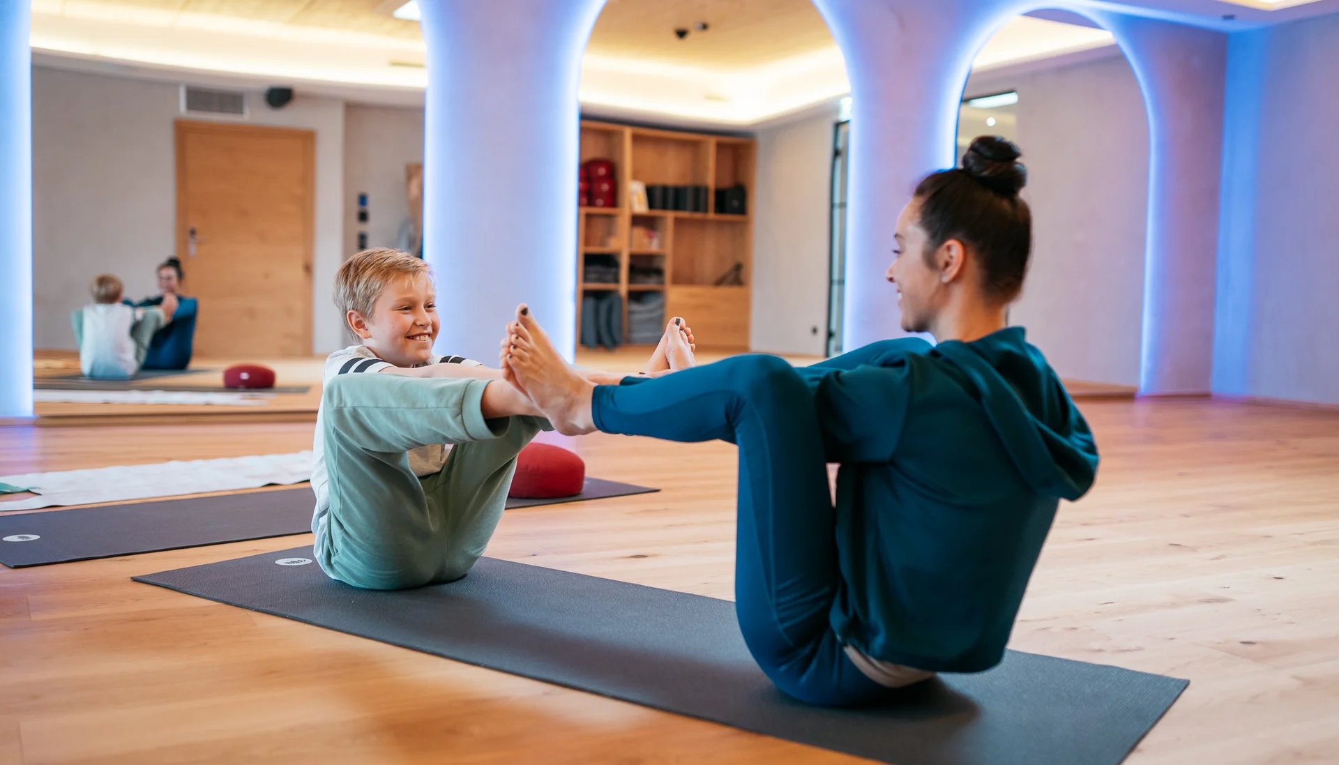 Ihr Hotel für Alleinerziehende Frau und Kind machen gemeinsam Yogaübungen auf Matten in einem Raum
