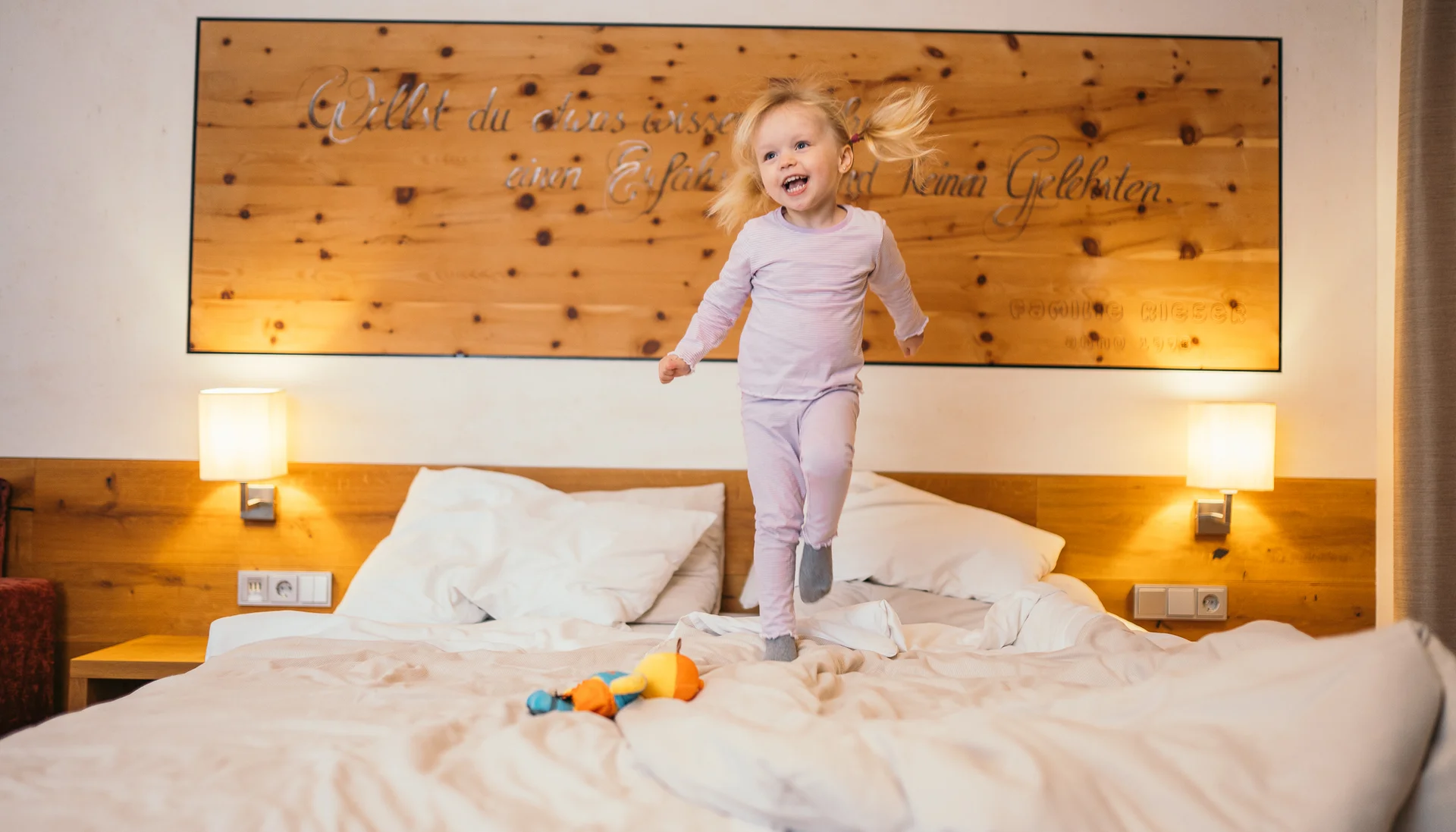 Zimmer und Angebote am Achensee Glückliches kleines Mädchen springt auf einem Bett in einem gemütlichen Schlafzimmer