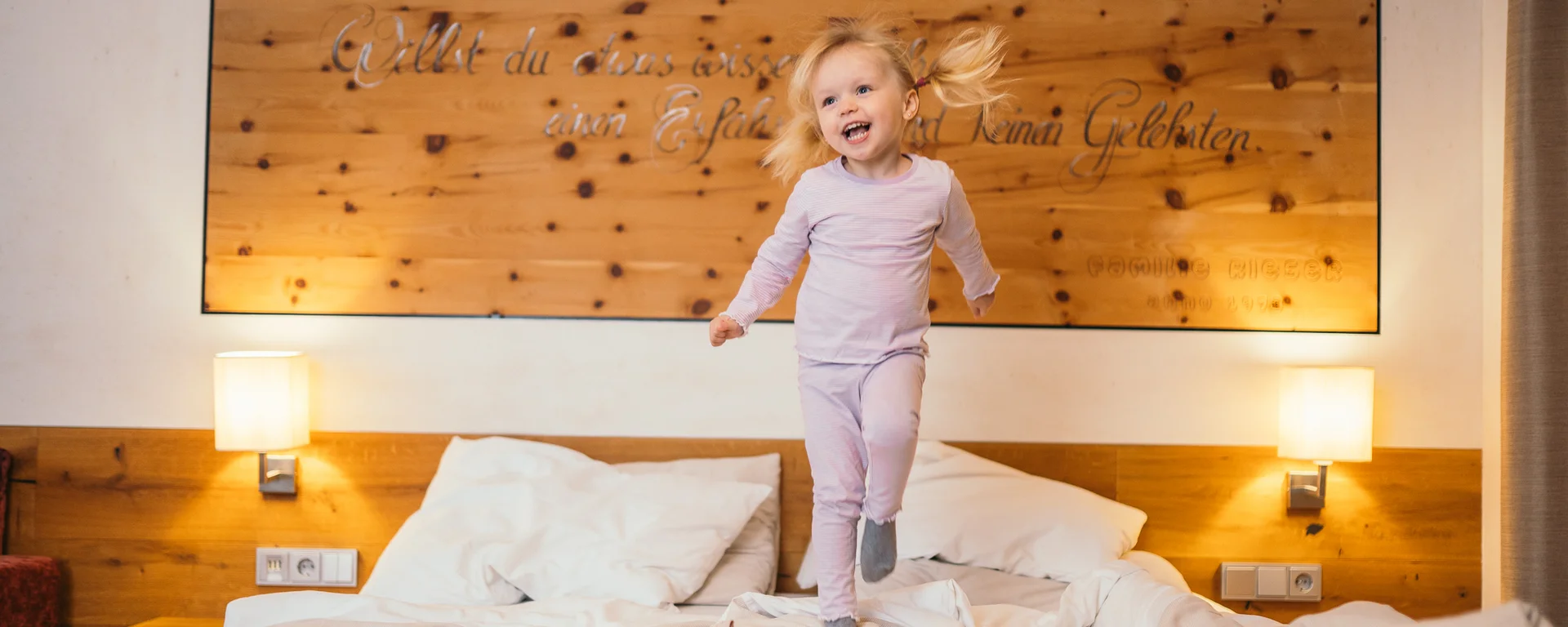 Ihr Hotel für Alleinerziehende Glückliches kleines Mädchen springt auf einem Bett in einem gemütlichen Schlafzimmer