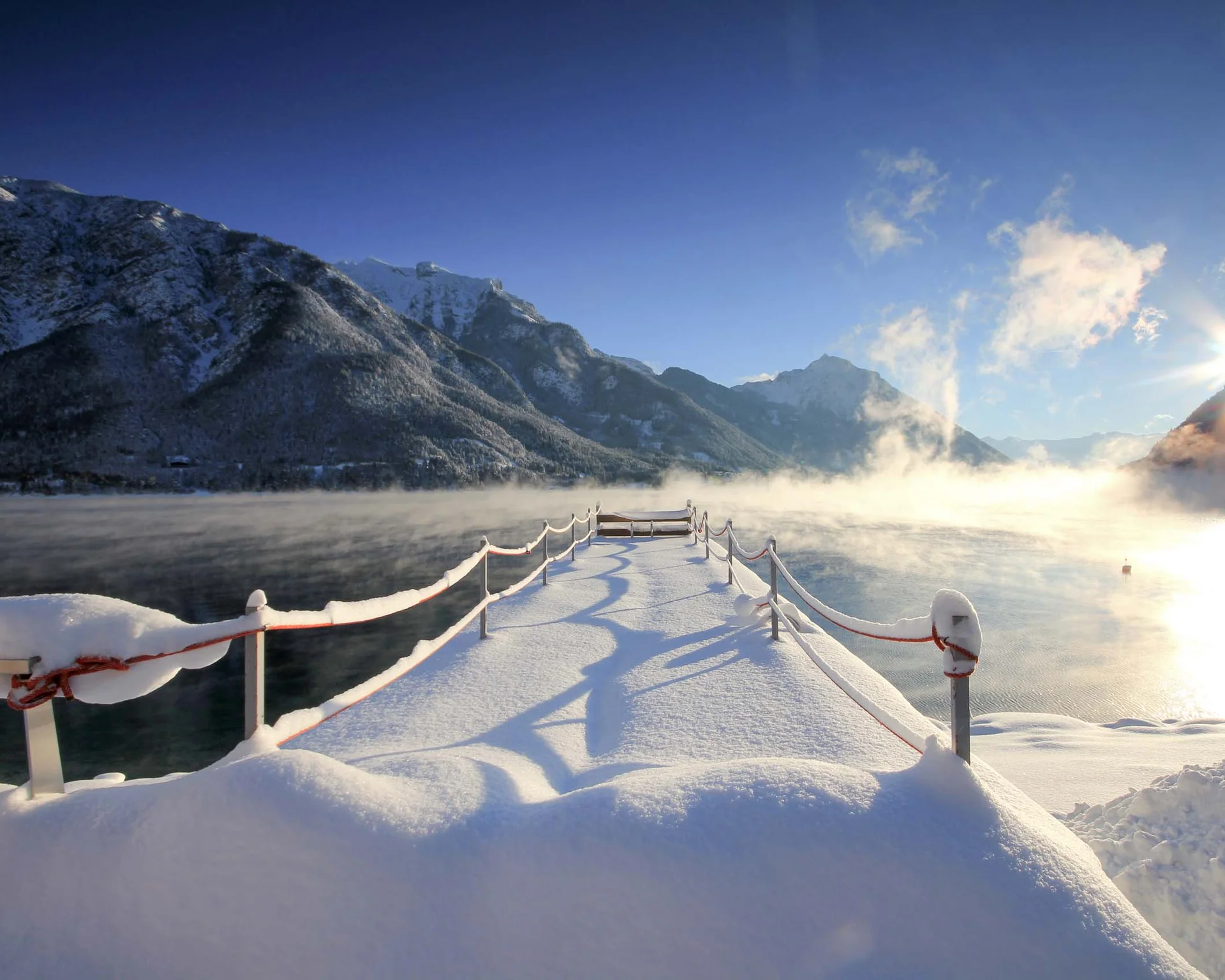 Ihr Rückzugsort in der Unterkunft am Achensee Verschneiter Steg am See mit Bergen und Sonne im Winter