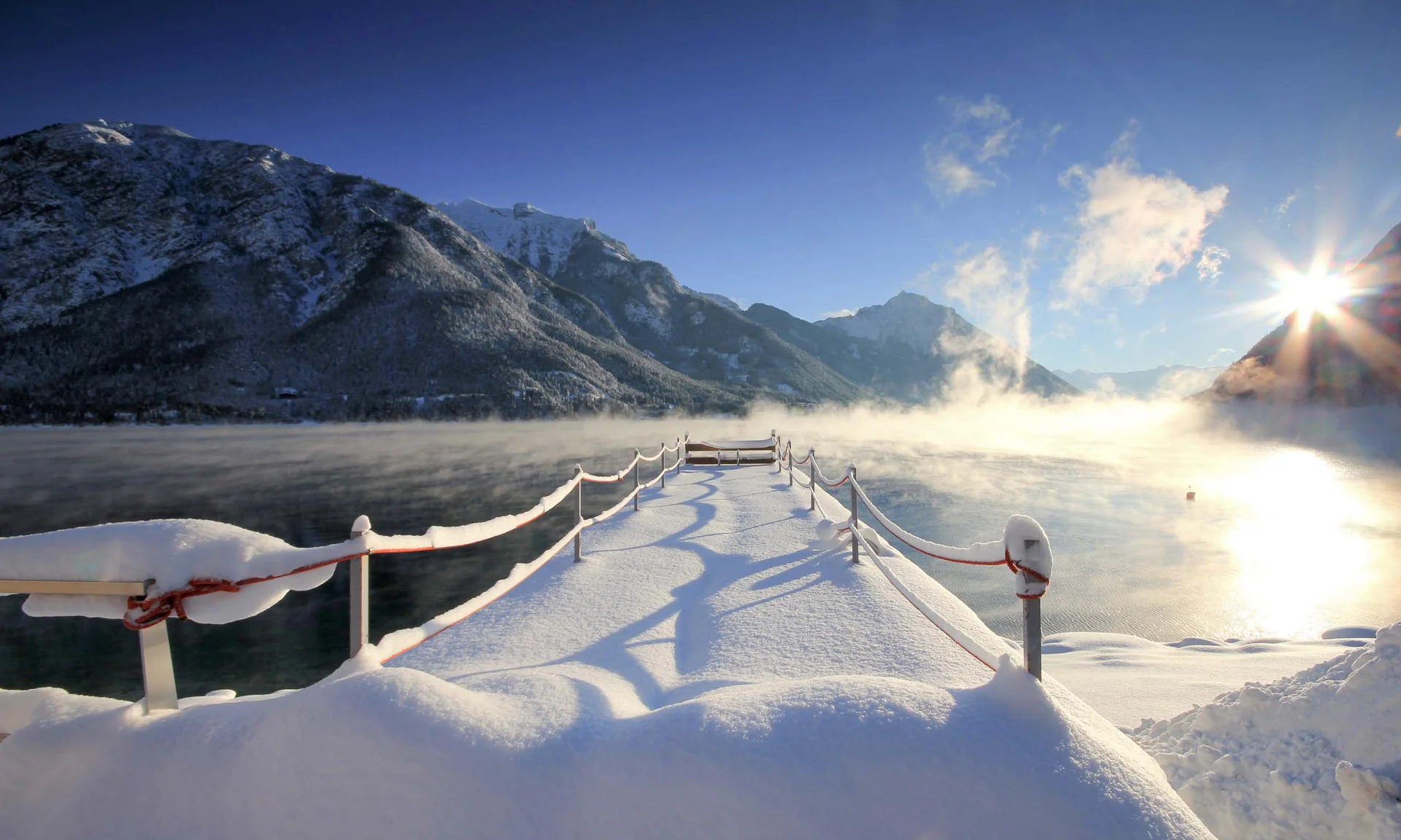 Your unforgettable active lakeside holiday in Austria Snow-covered pier on lake with mountains and sun in winter