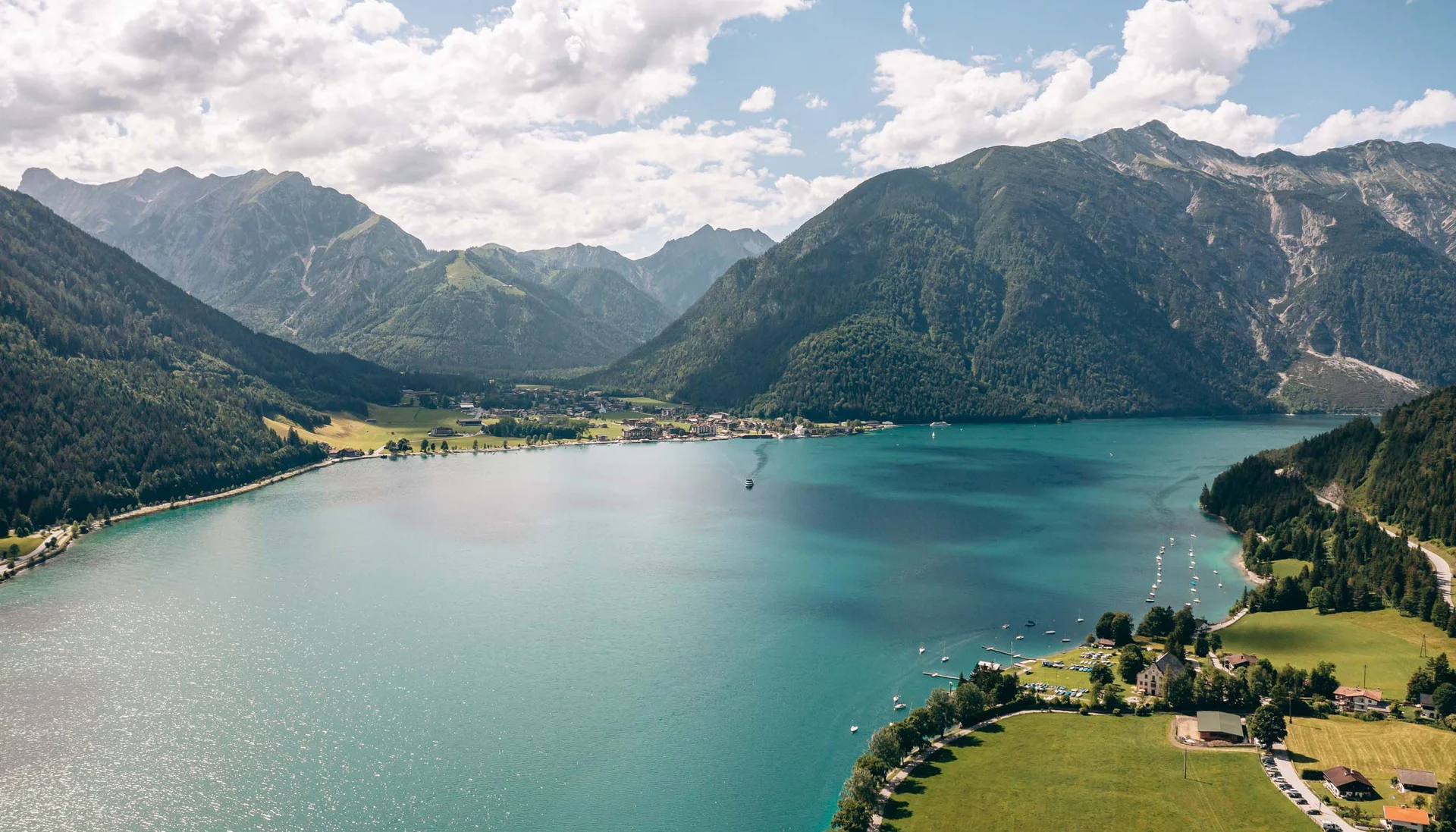 Outdoorspaß im Familienhotel am See in Österreich Bergsee mit klaren blauen Wasser, umgeben von grünen Bergen und Dorf am Ufer
