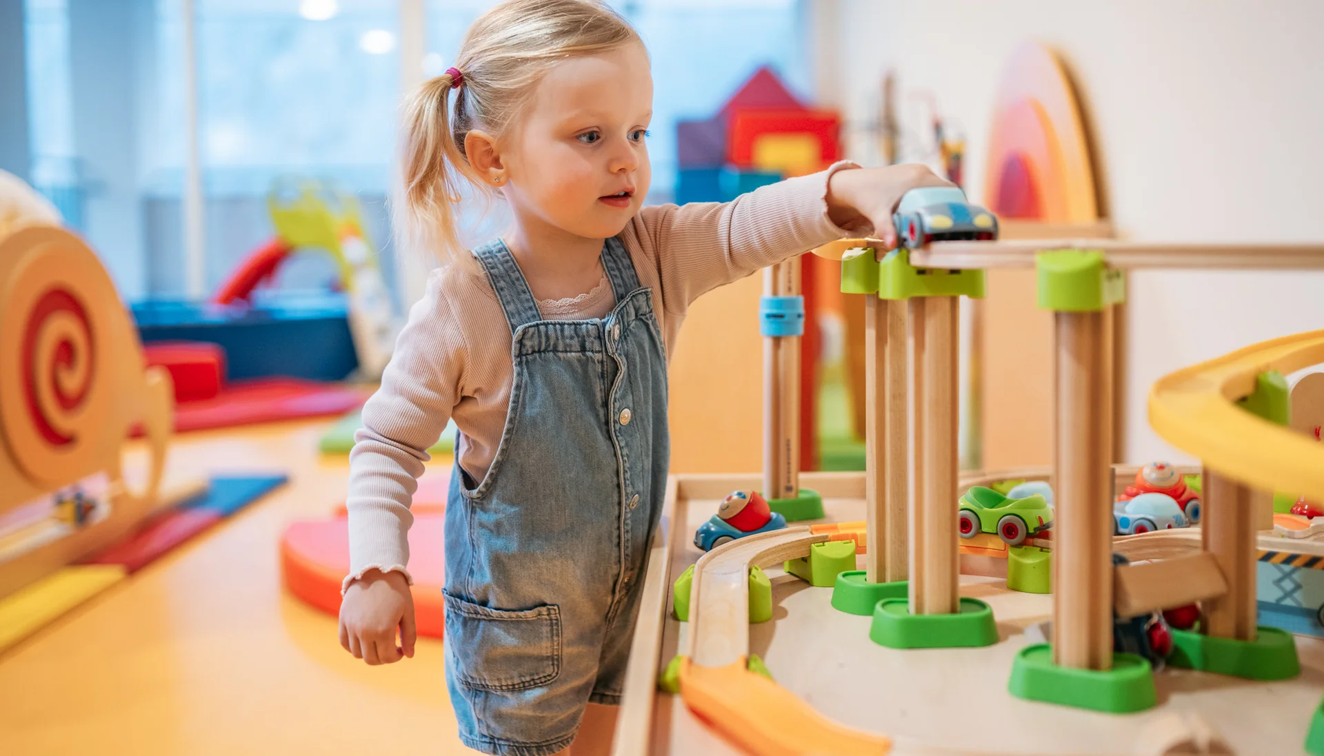 Urlaub im Hotel mit Indoorspielplatz Kleines Mädchen spielt mit einer Holzeisenbahn im Spielzimmer