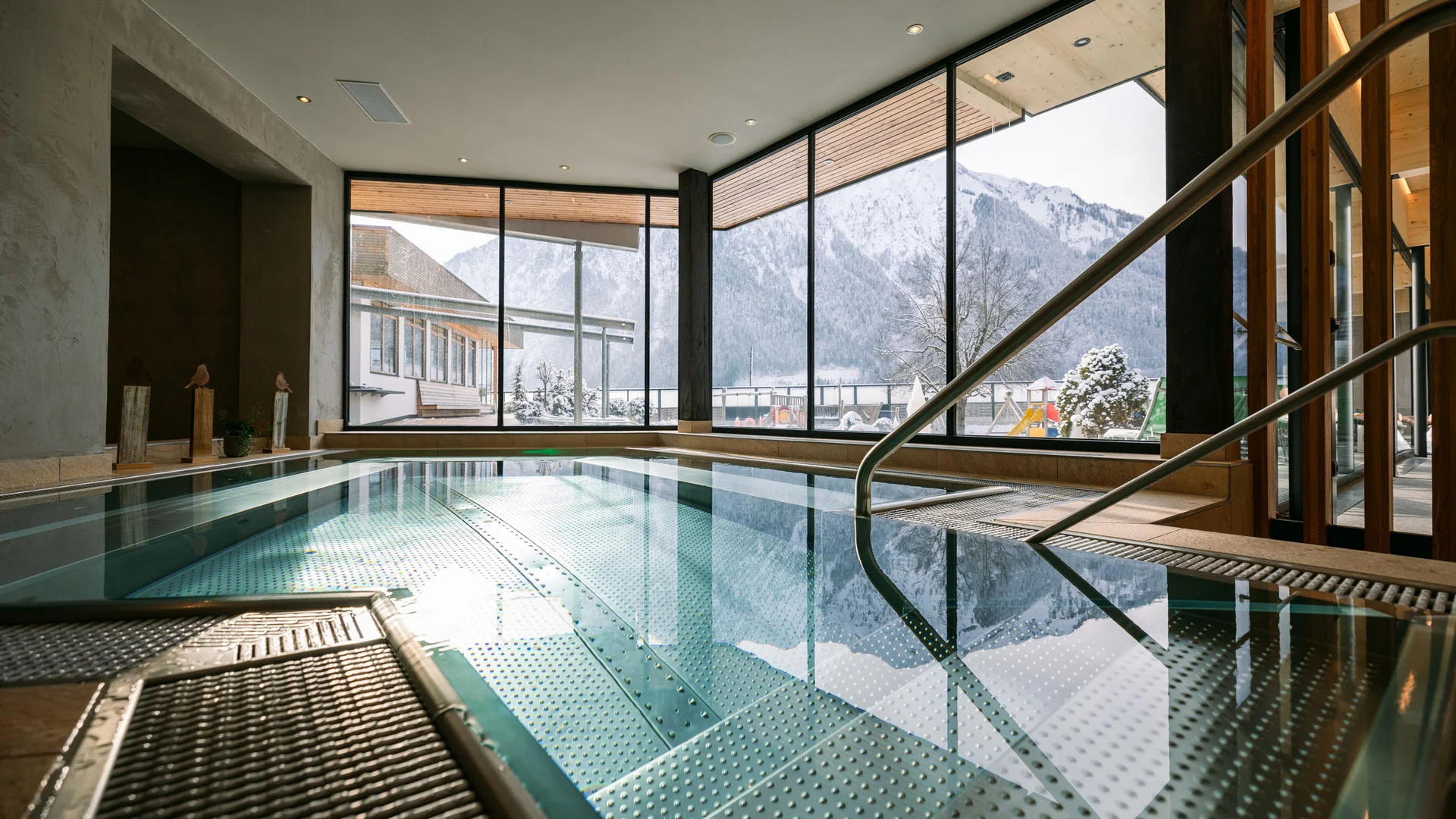 Wasserspaß im Familienhotel in Tirol mit Pool Innen-Schwimmbad mit großen Fenstern und Blick auf verschneite Berge