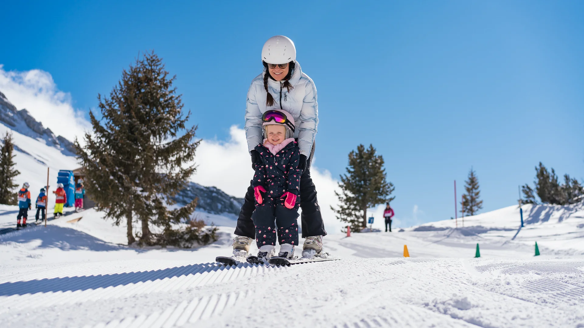 Familienzeit im Kinderhotel Buchau am Achensee Erwachsene und Kind lernen gemeinsam Skifahren auf verschneiter Piste bei sonnigem Wetter
